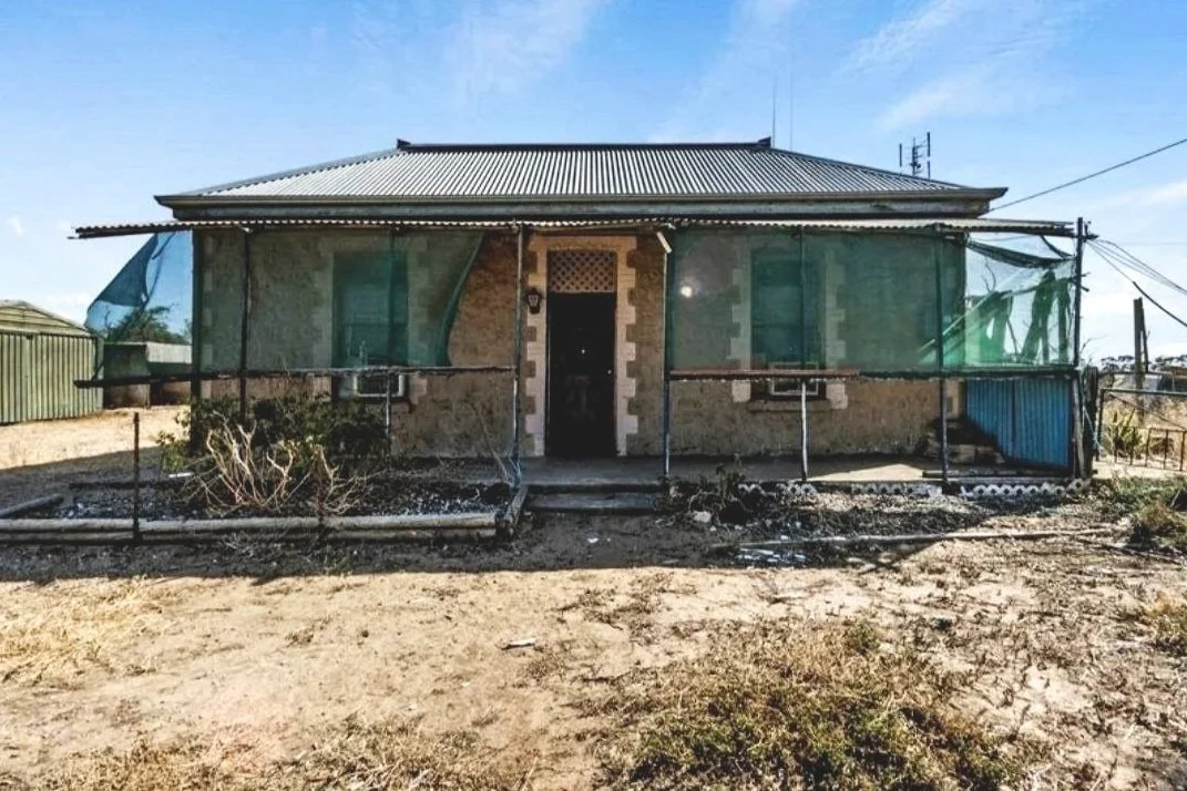 A small house under construction or renovation, with scaffolding around it, a metal roof, and an unfinished exterior wall.