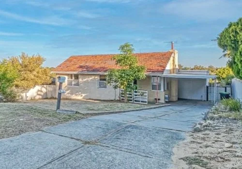 A house with a red-tiled roof, a driveway, and some trees and bushes in the yard.