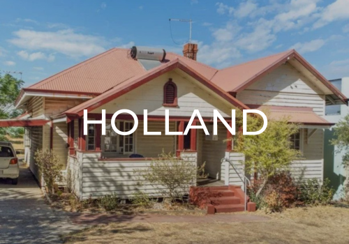 A house with a red-tiled roof, cream-colored wooden siding, red shutters, a front porch, and a small staircase. The house is set on a yard with trees and bushes, under a partly cloudy sky.