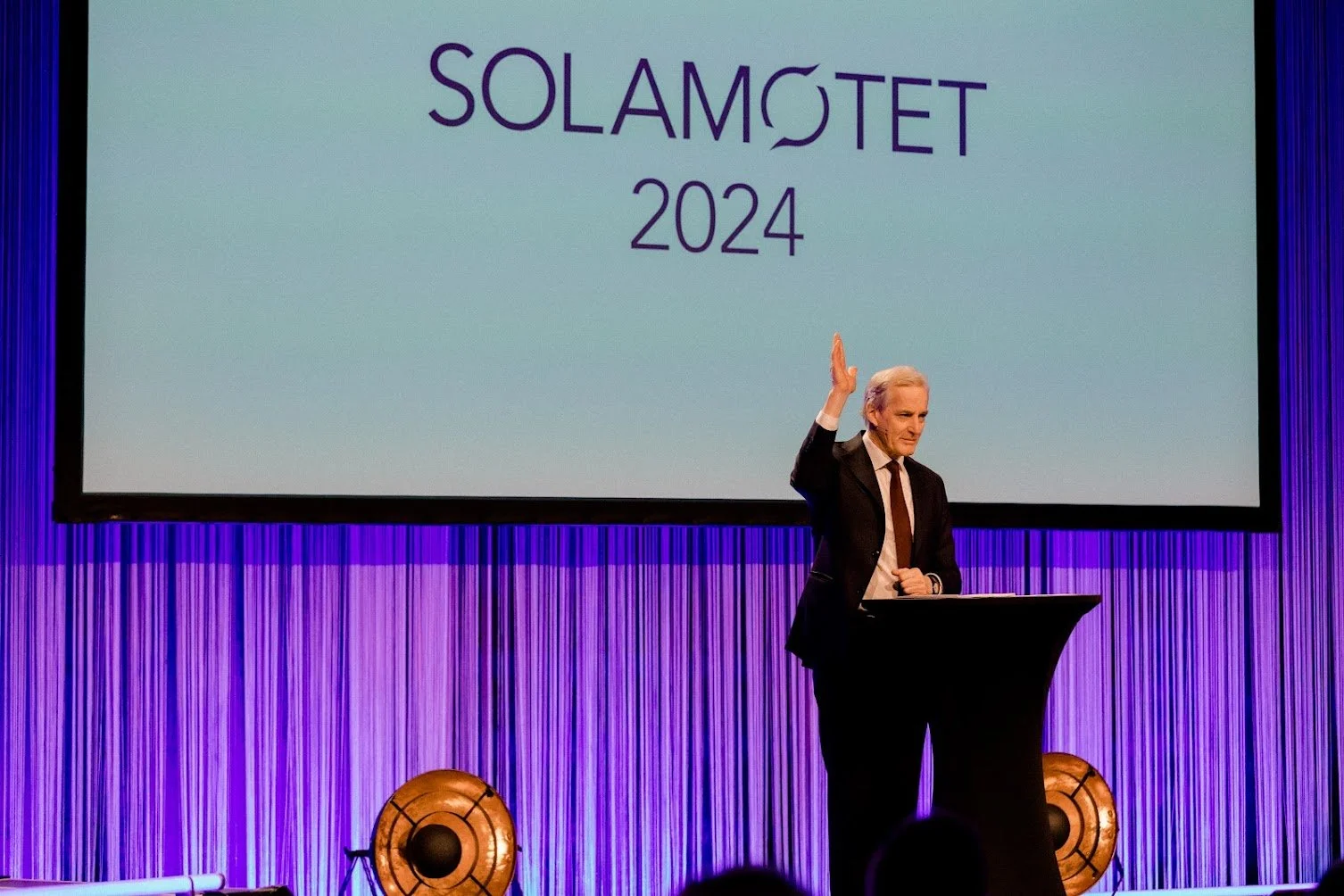 En mann i svart dress holder et foredrag på en konferanse med en stor skjerm som viser teksten "SOLAMØTET 2024".