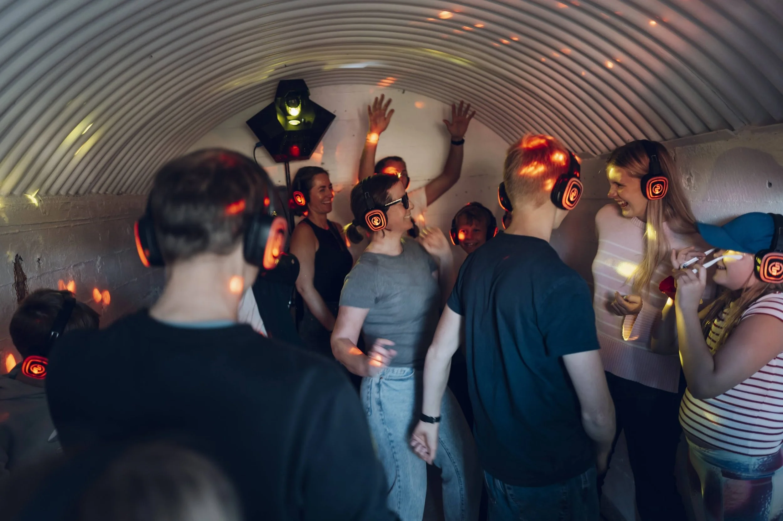 Folk har det gøy i en liten, buktende festhule med DJ-utstyr, der de danser og prater under fargede lys.