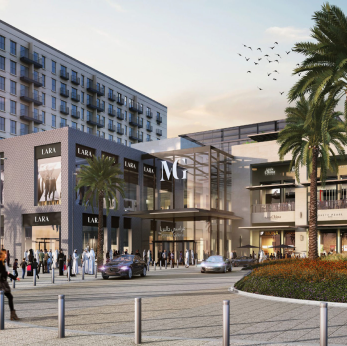Modern shopping center with luxury stores, palm trees, parked cars, and pedestrians at sunset.