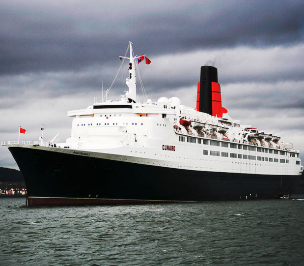 A large white cruise ship named Cunard sailing on water under cloudy skies, with a black and red funnel.