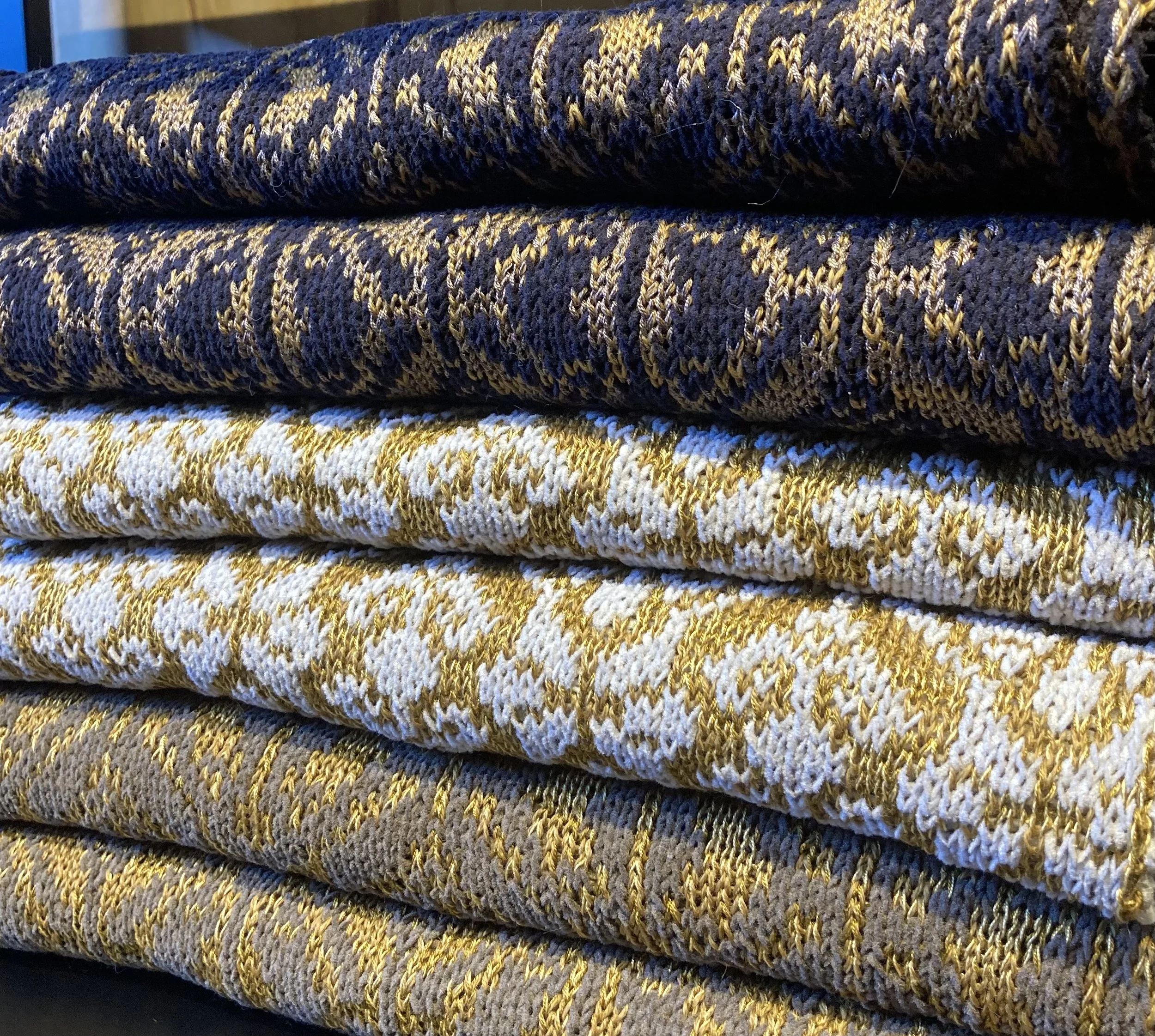 Stack of Studio Myr jacquard knitwear in black, gold and beige — folded sustainable Merino and cotton blend pieces.