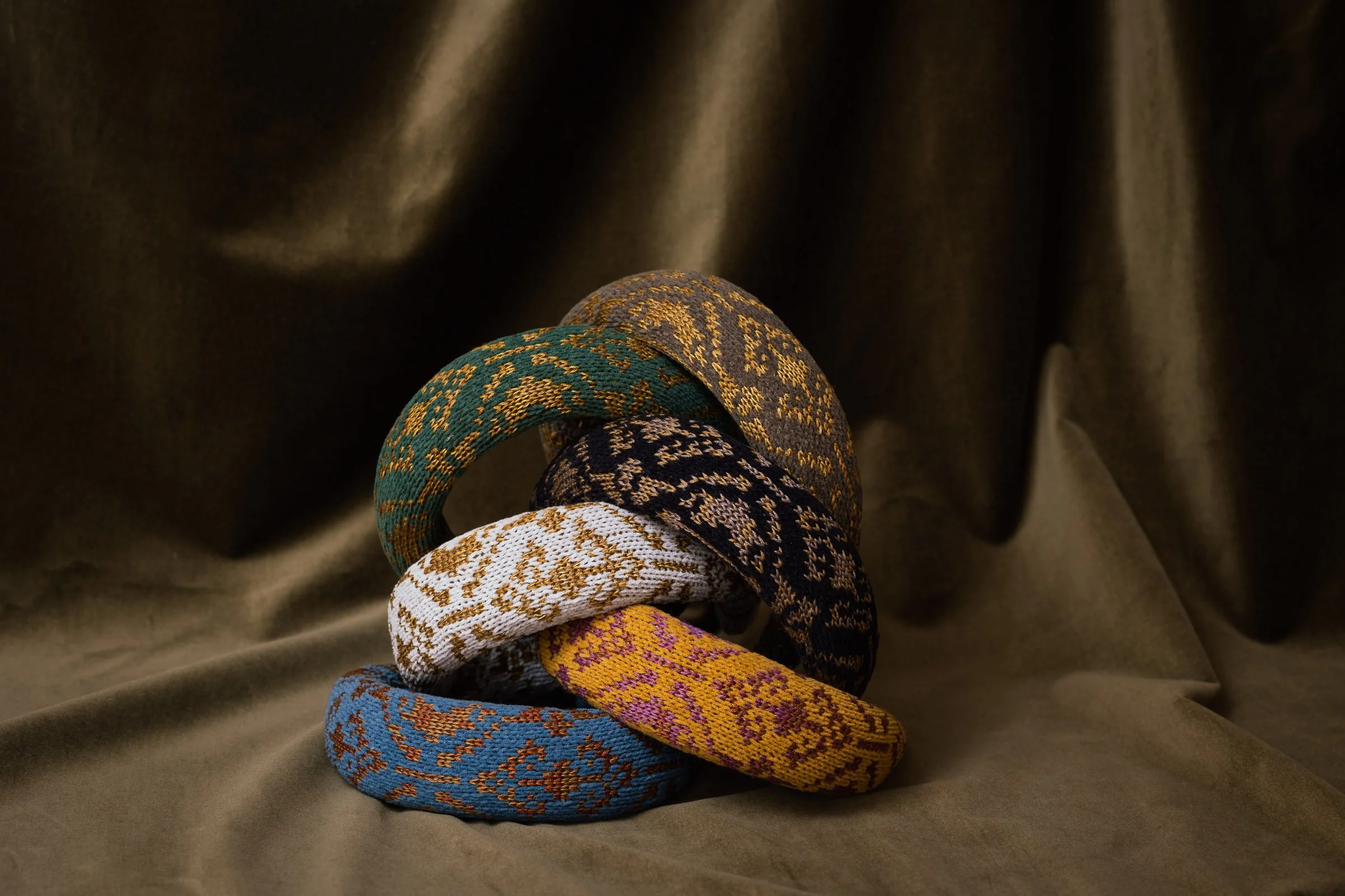 Stack of six knitted velvet diadems in different colours displayed on a brown draped fabric — Studio Myr Velvet Collection