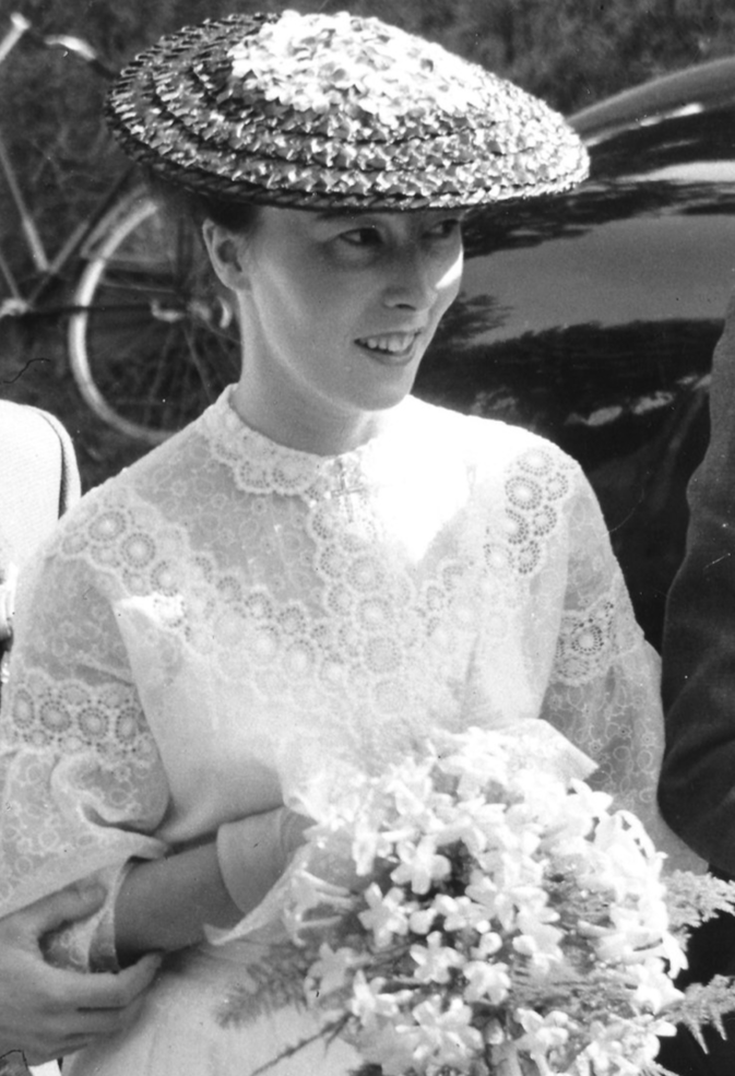 Black-and-white photograph of the founder’s mother as a young bride, wearing a lace dress and hat, holding a bouquet on her wedding day