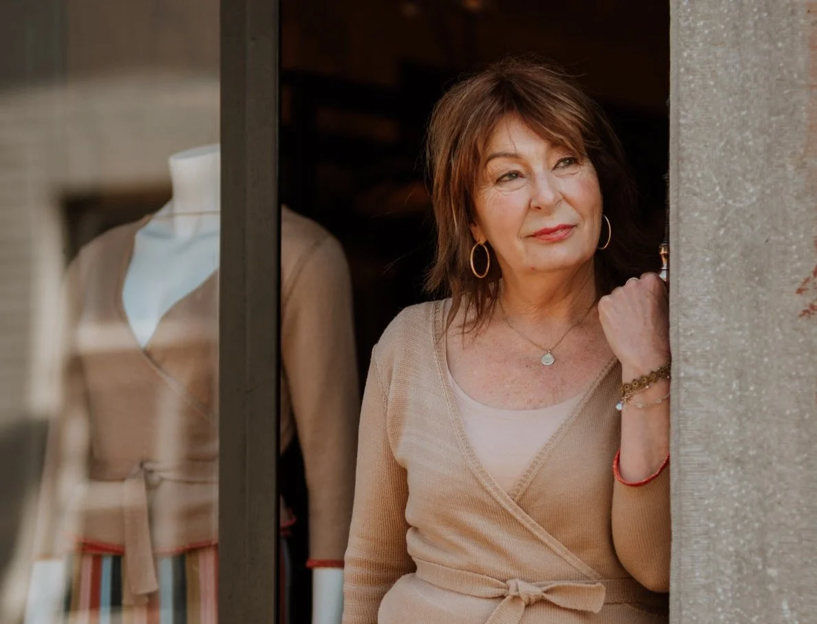 Studio Myr designer Miriam Lenarts standing in her boutique doorway, wearing her own knitwear — reflecting a personal, nature-aligned commitment to slow fashion.