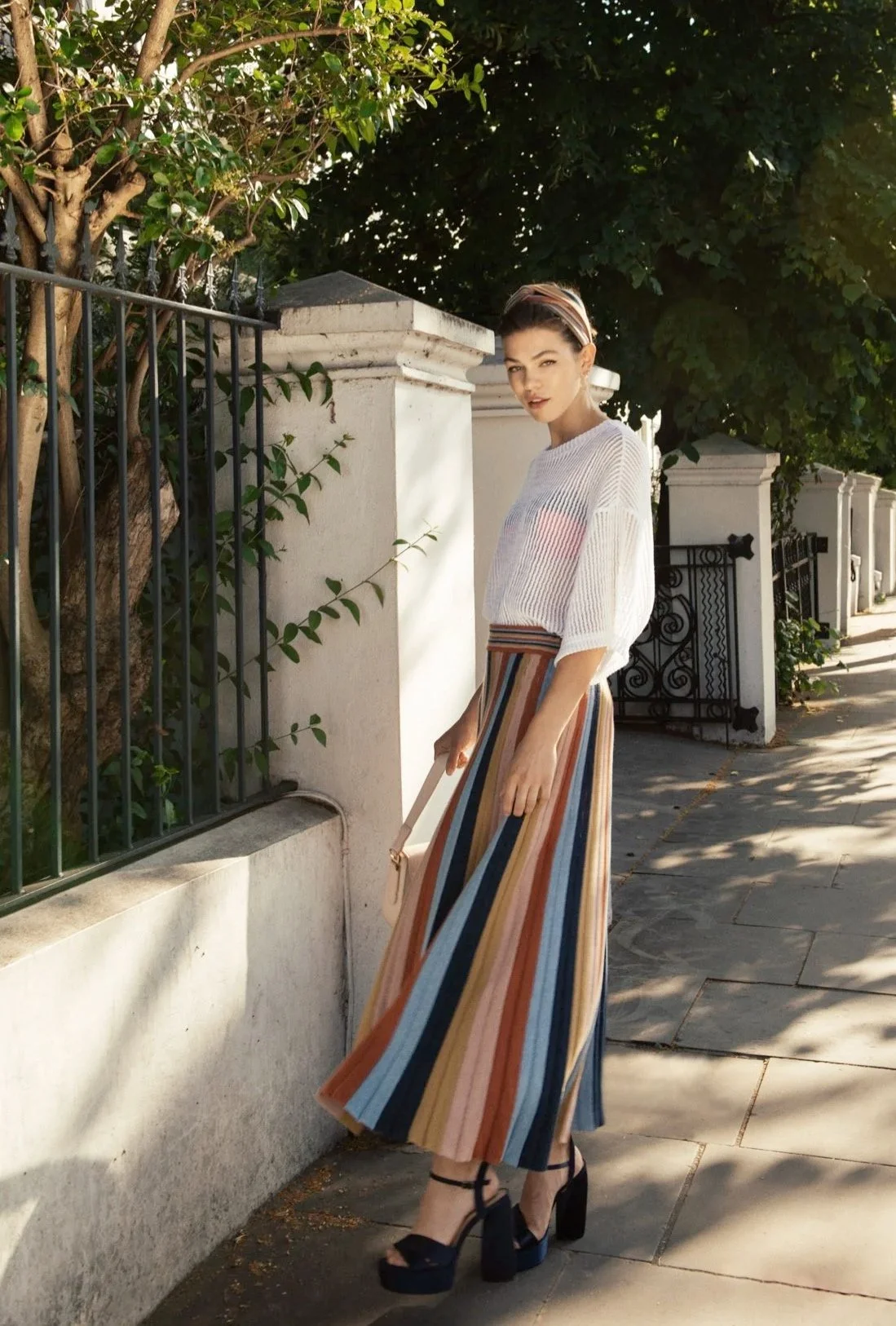 Woman wearing a white knit top and the Denîmes striped skirt of Studio Myr, styled with ease in an urban setting, highlighting contrast, movement, and feminine silhouettes.
