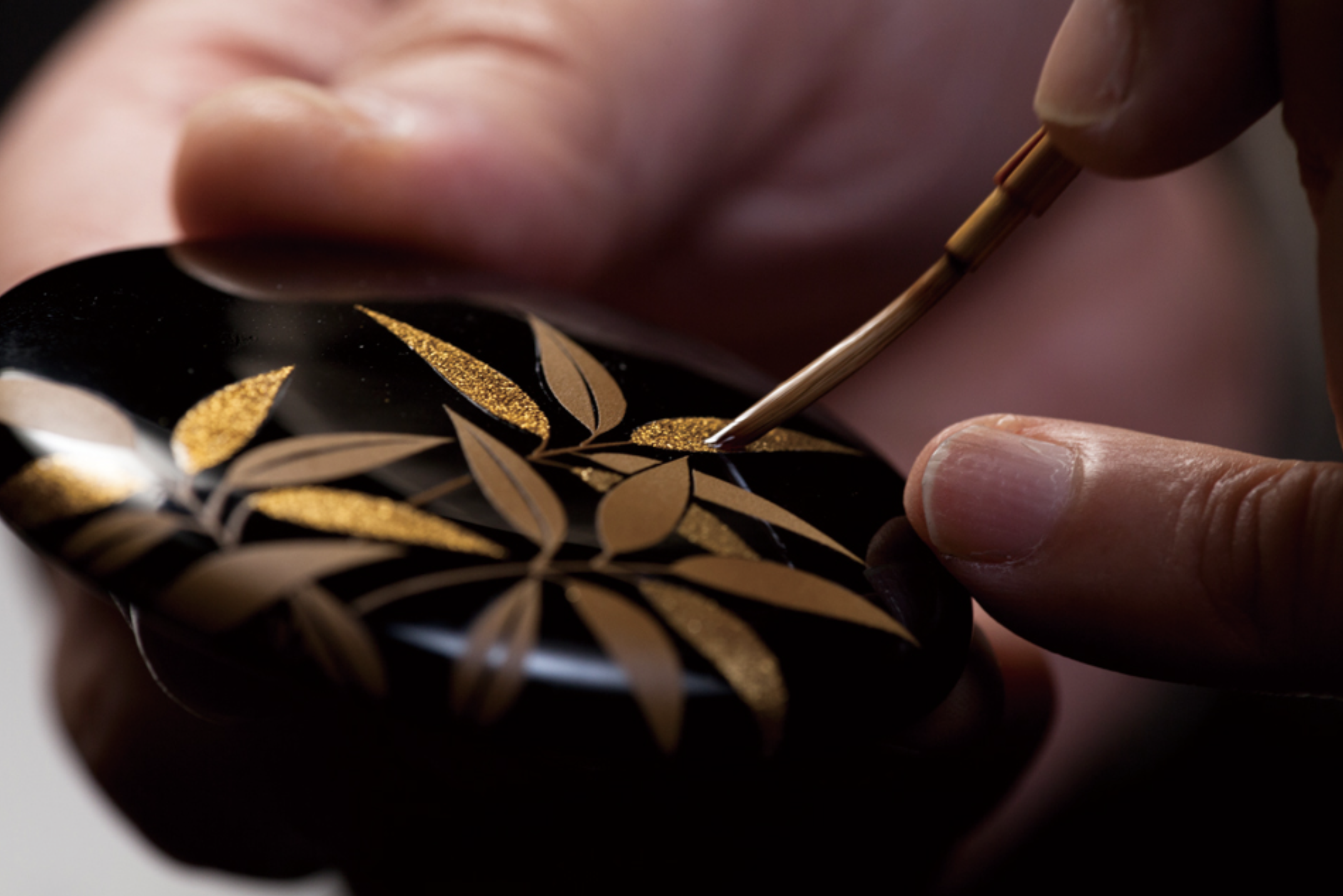 Hands decorating Japanese lacquerware with gold motifs, demonstrating precision, patience, and centuries-old craft traditions
