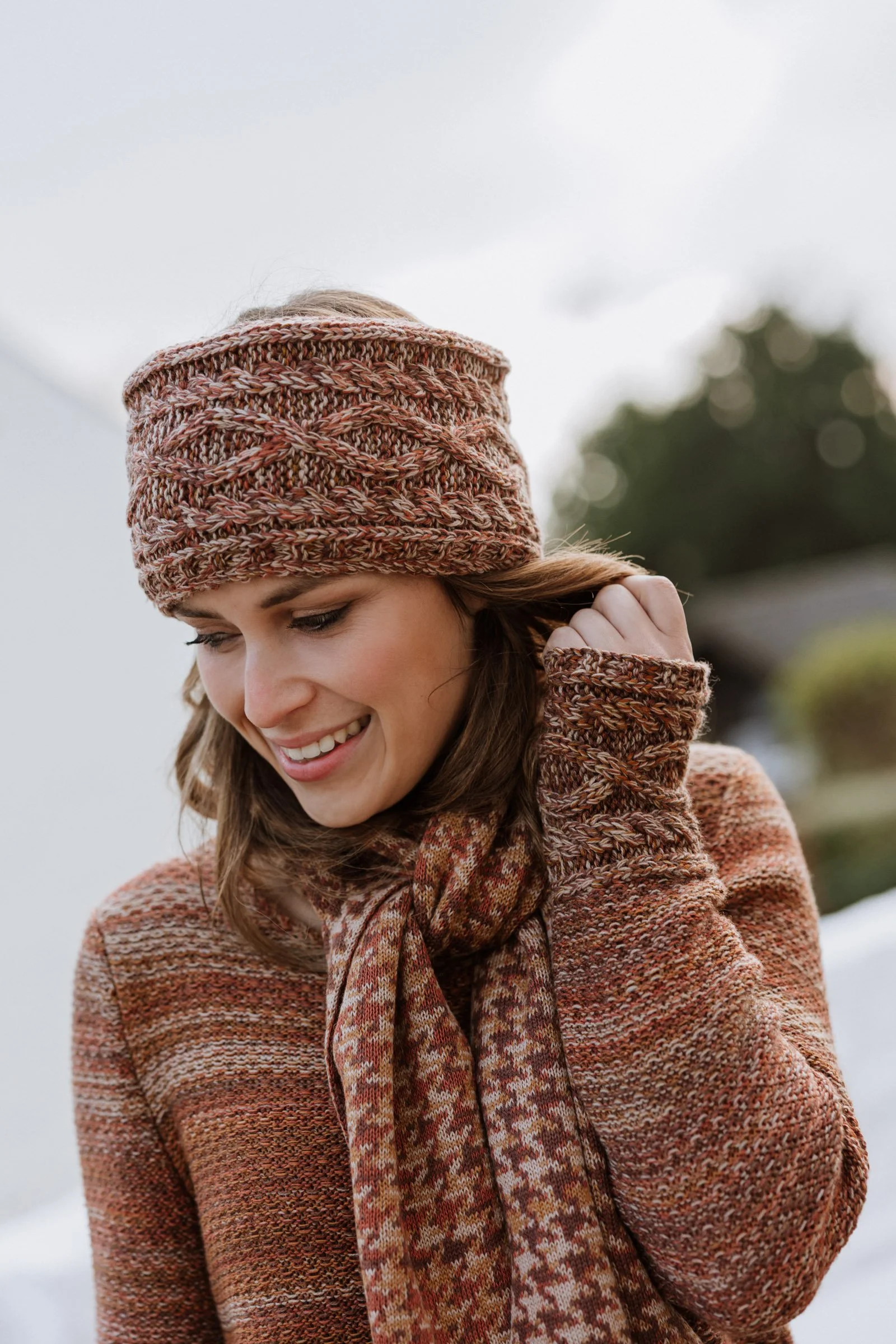 Model wearing a Studio Myr knitted headband and matching scarf in warm earthy tones, styled outdoors in natural light.