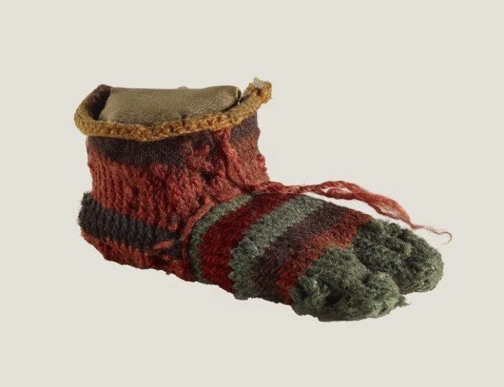 4th-century Coptic child’s sock from Egypt, crafted in wool with a split toe for wearing in sandals, worked in multiple coloured yarns and showcasing early needle-binding techniques.