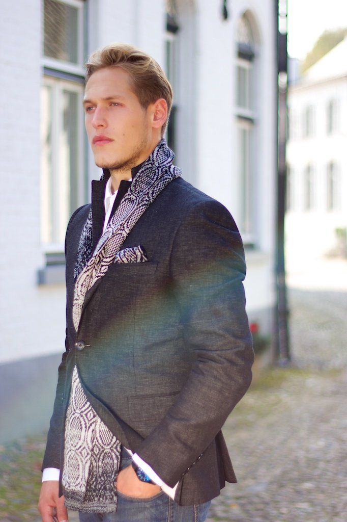 Male model wearing an elegant jacquard knit scarf from Studio Myr, styled with tailored summer layering in soft natural light, reflecting refined craftsmanship and quiet luxury.
