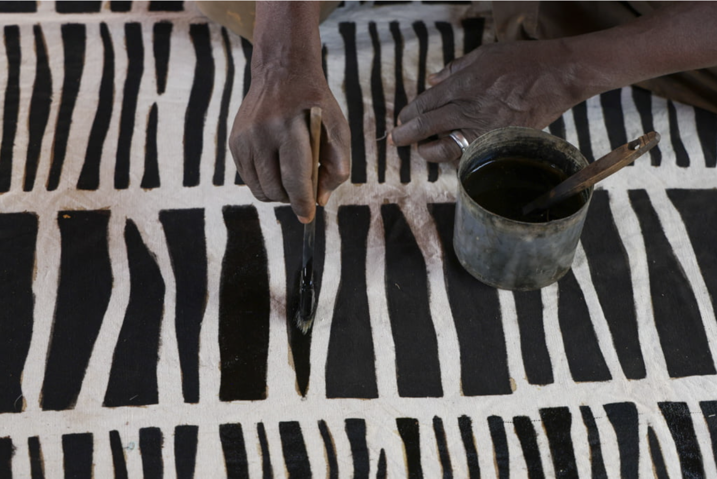 Hands painting Bogolan mud cloth in Mali, illustrating ancestral textile knowledge passed through repetition and practice.