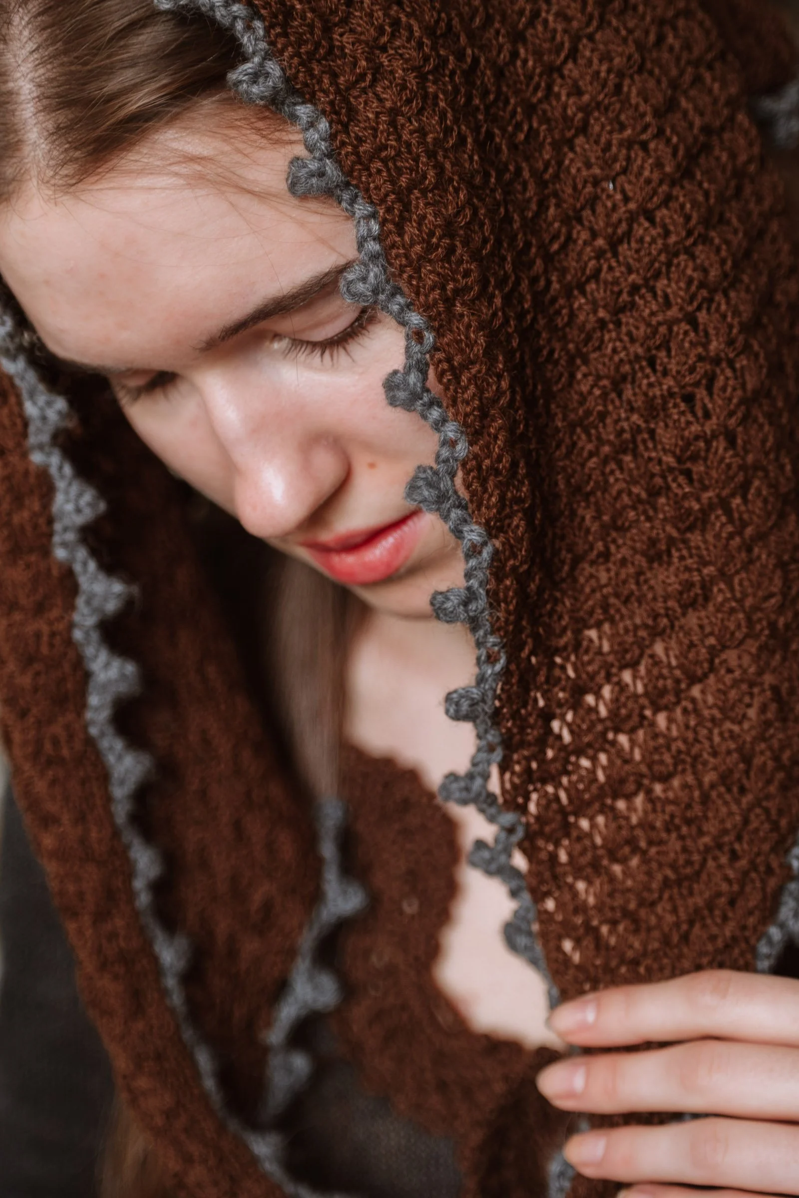 Close-up of the Francisca triangular headscarf in chocolate brown Merino wool, showing the delicate charcoal grey hand-crocheted edging framing the model's face.