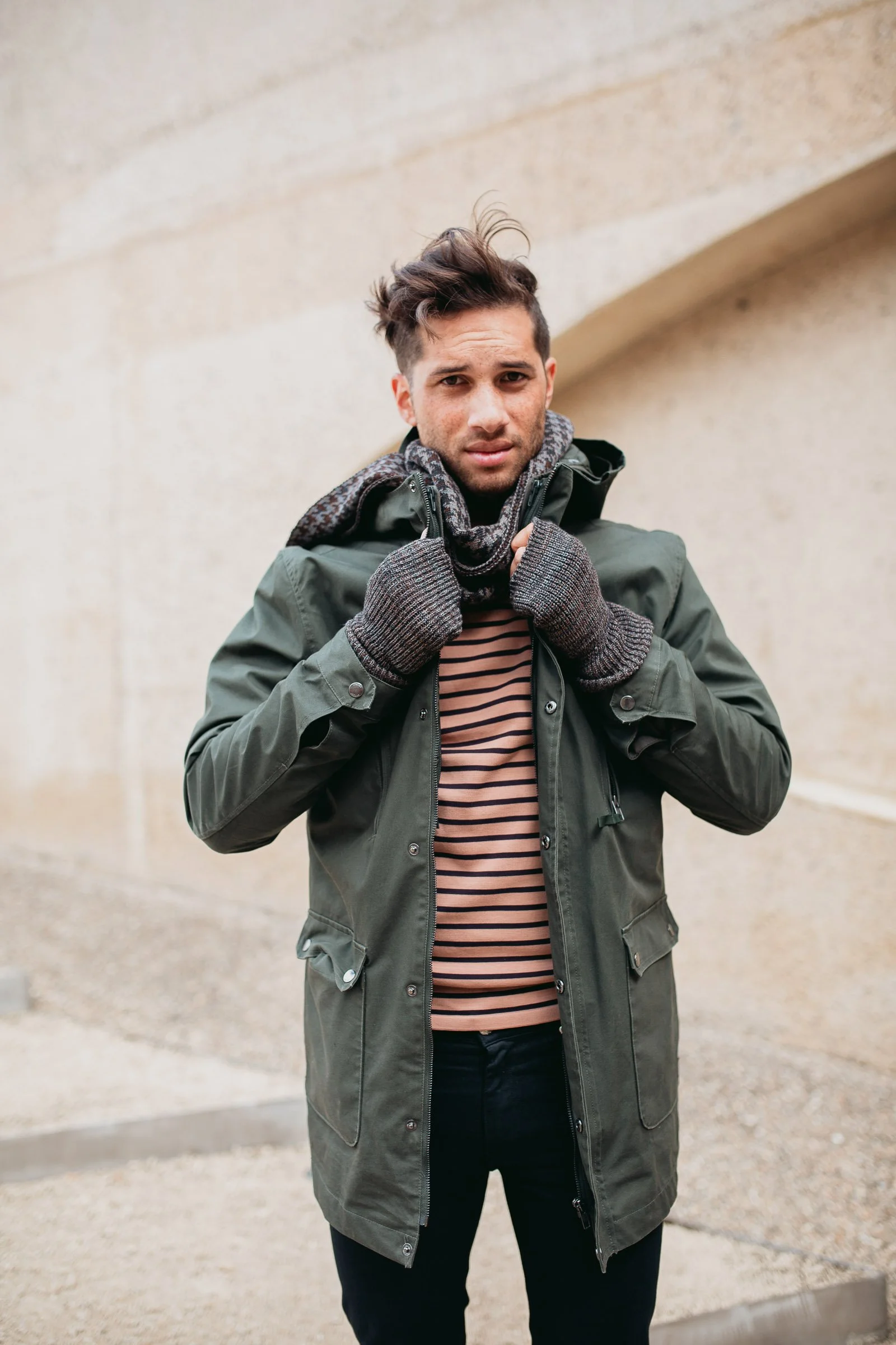 Young man in a green jacket and striped shirt adjusting his hood outdoors