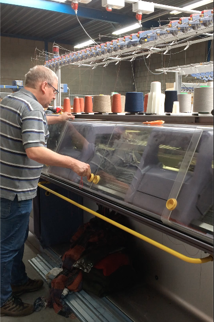 Knitter operating an industrial knitting machine in a Dutch factory, producing garments for Studio Myr using traditional knitwear techniques.