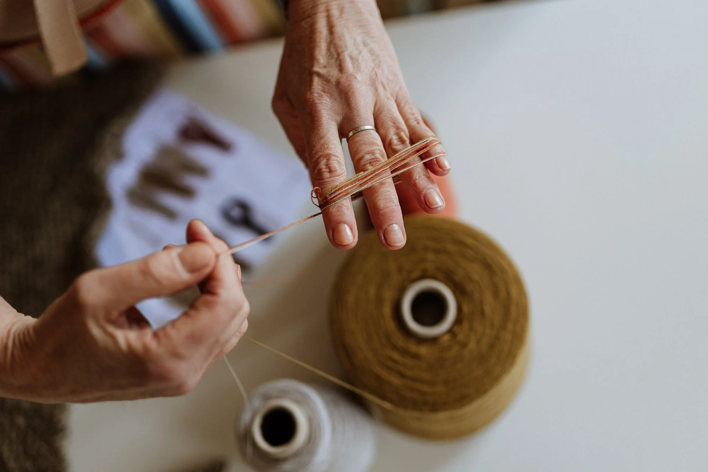 Close-up of hands handling yarn and thread, reflecting the tactile process of craftsmanship and material exploration.