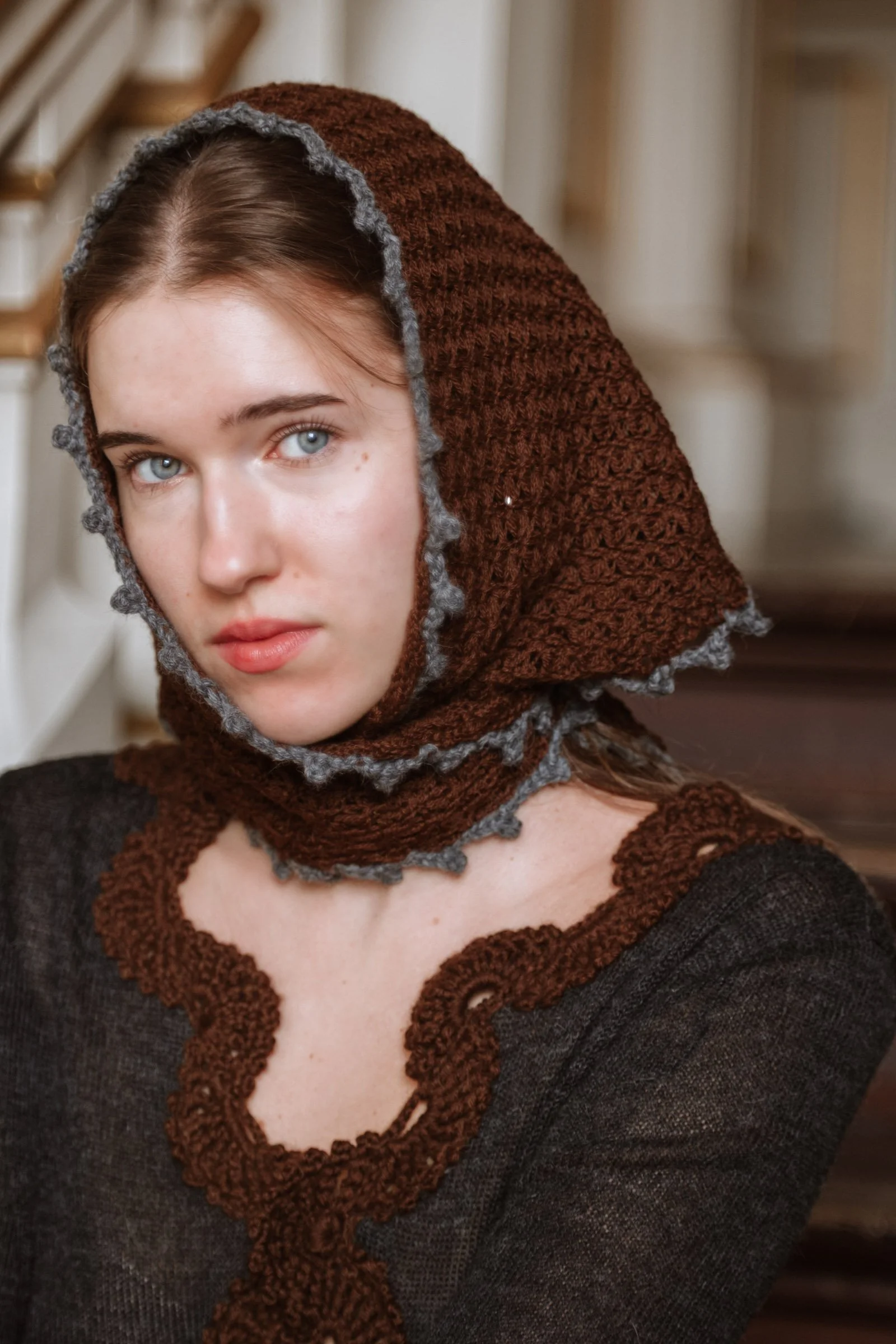 Model wearing the Francisca triangular scarf as an elegant headscarf, featuring rich chocolate brown knit, contrasting charcoal grey crochet edging and a decorative button closure.