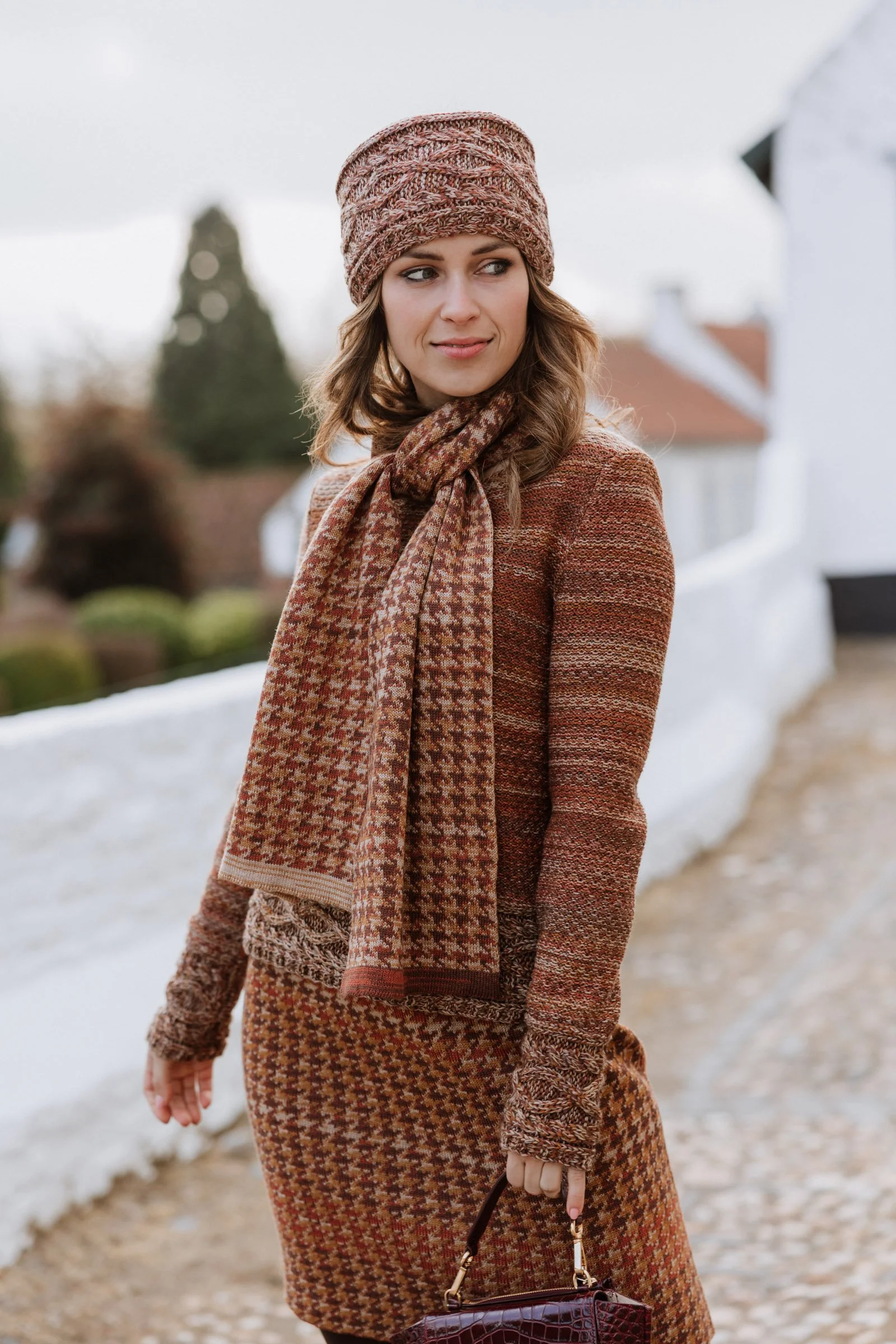 Model wearing a Studio Myr knitted scarf and skirt in warm pied-de-poule tones, styled outdoors.