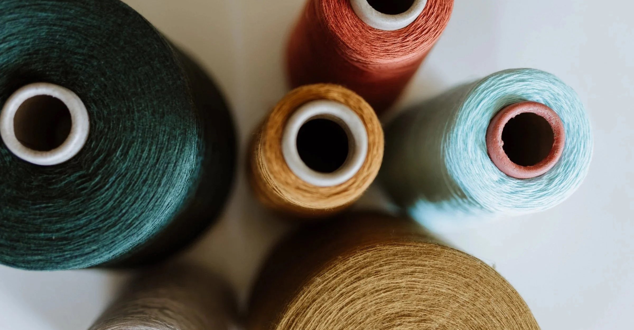 Spools of natural yarn in soft green, ochre, terracotta, and pale blue tones, reflecting Studio Myr’s commitment to pure materials and slow craftsmanship.