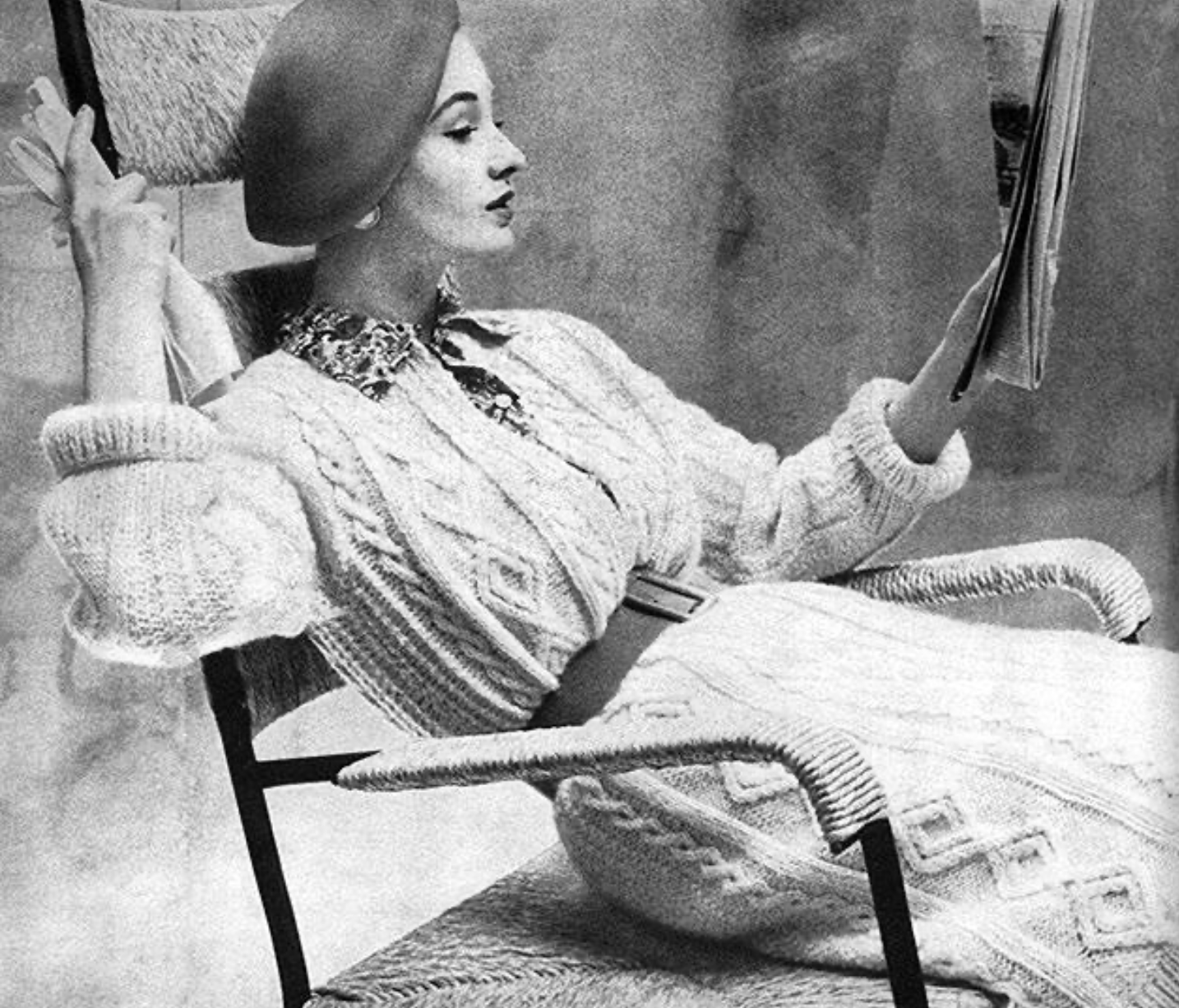 Fashion model sitting in a chair, wearing an Aran-inspired long cardigan by Digby Morton - 1960