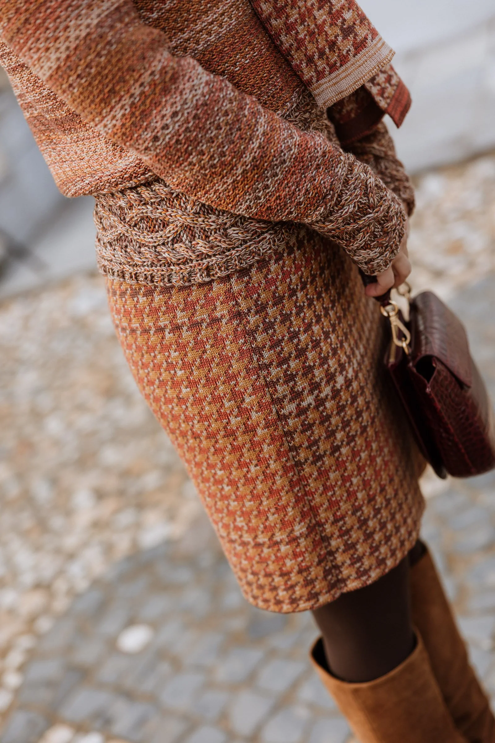 Detail of model wearing a Studio Myr knitted skirt in a refined pied-de-poule structure, photographed on stone steps.