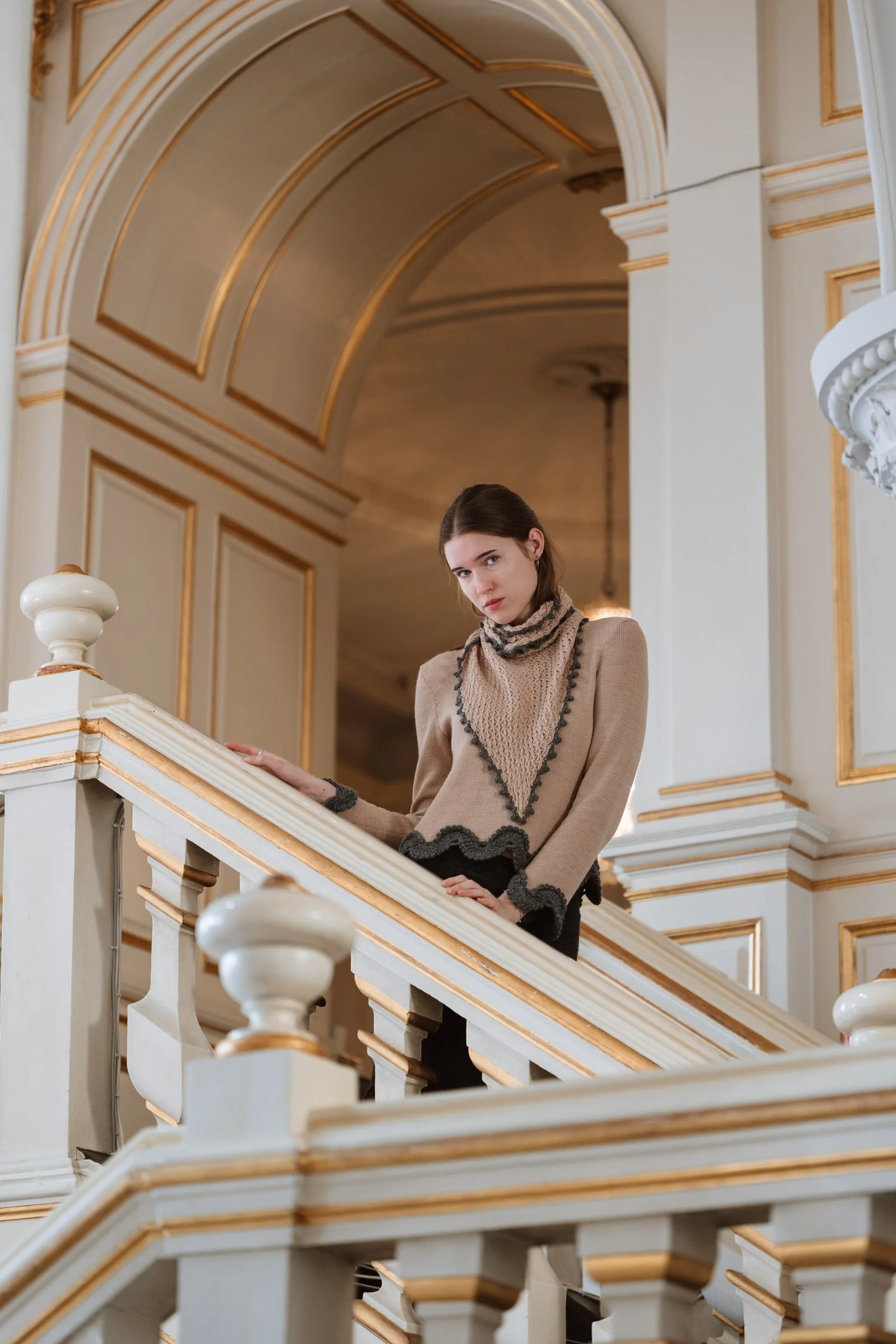 Model wearing the Gabriella triangular scarf in beige and grey, elegantly tied around the neck with its delicate hand-crocheted edging visible