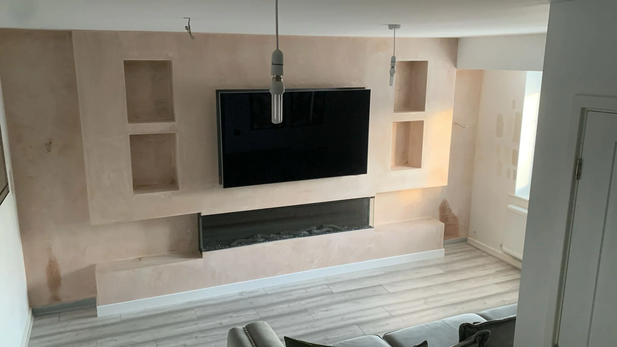 Living room with a built-in beige wall with four open shelves, a black flat-screen TV, a modern fireplace below the TV, and two hanging light fixtures.