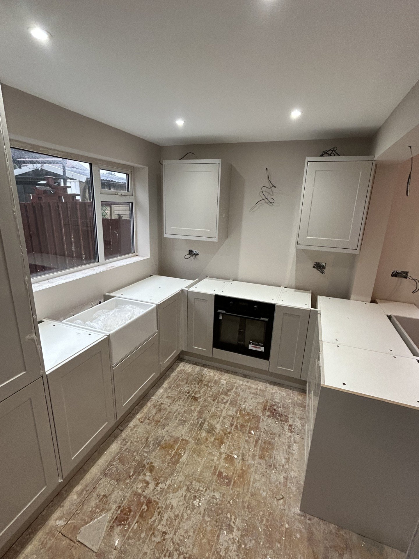 Kitchen under renovation with unfinished cabinets, exposed wiring, and a hardwood floor.