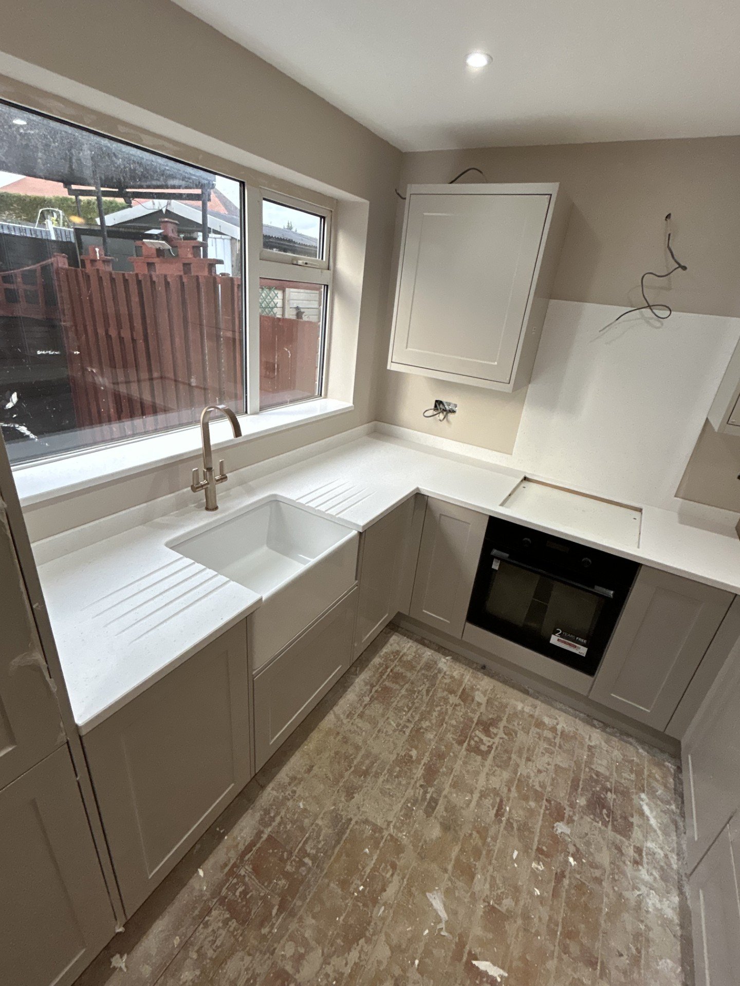 A kitchen with white cabinets, a sink under a large window, a built-in oven, and exposed wiring.