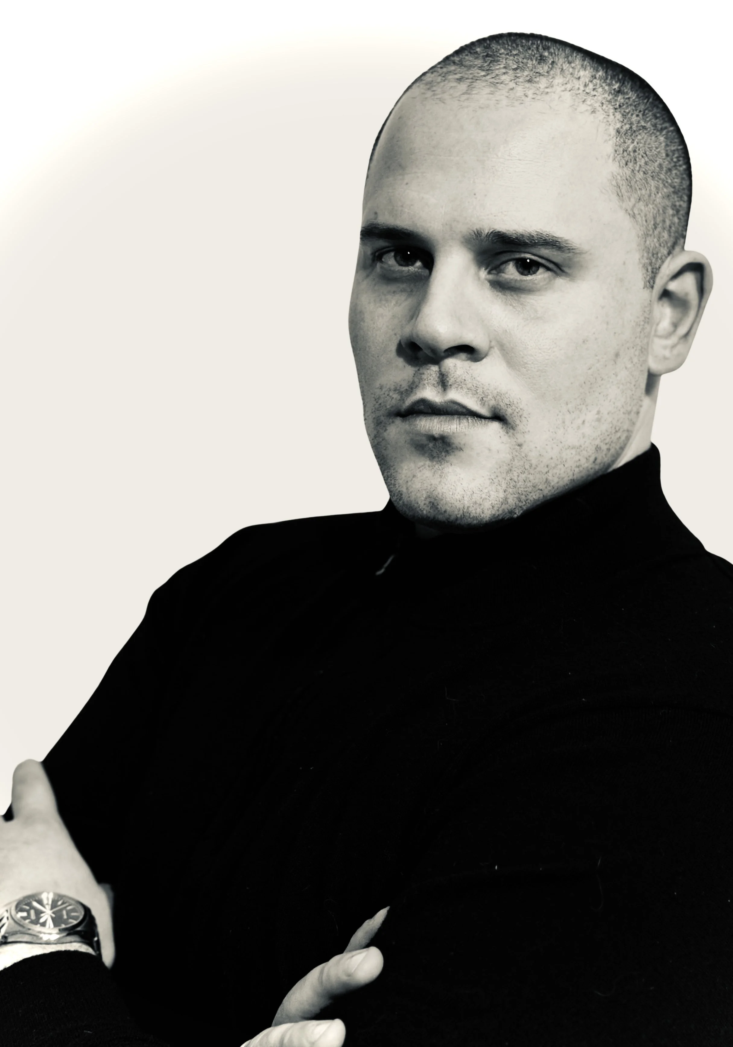 Portrait of a man with a shaved head wearing a black shirt and a watch, posing with arms crossed.