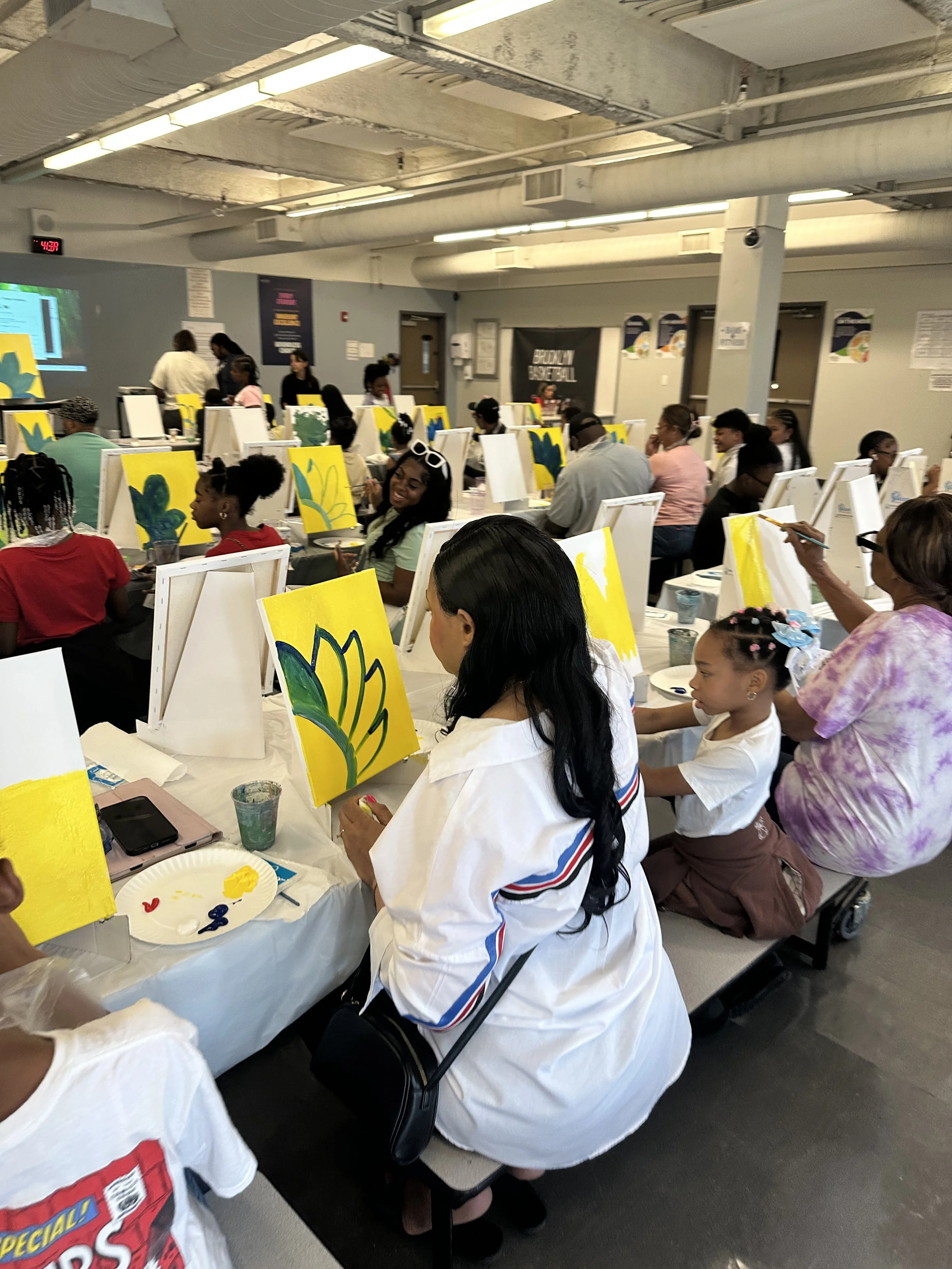 Participants painting yellow floral canvases during a ColorsintheDark school-based painting workshop in NYC.
