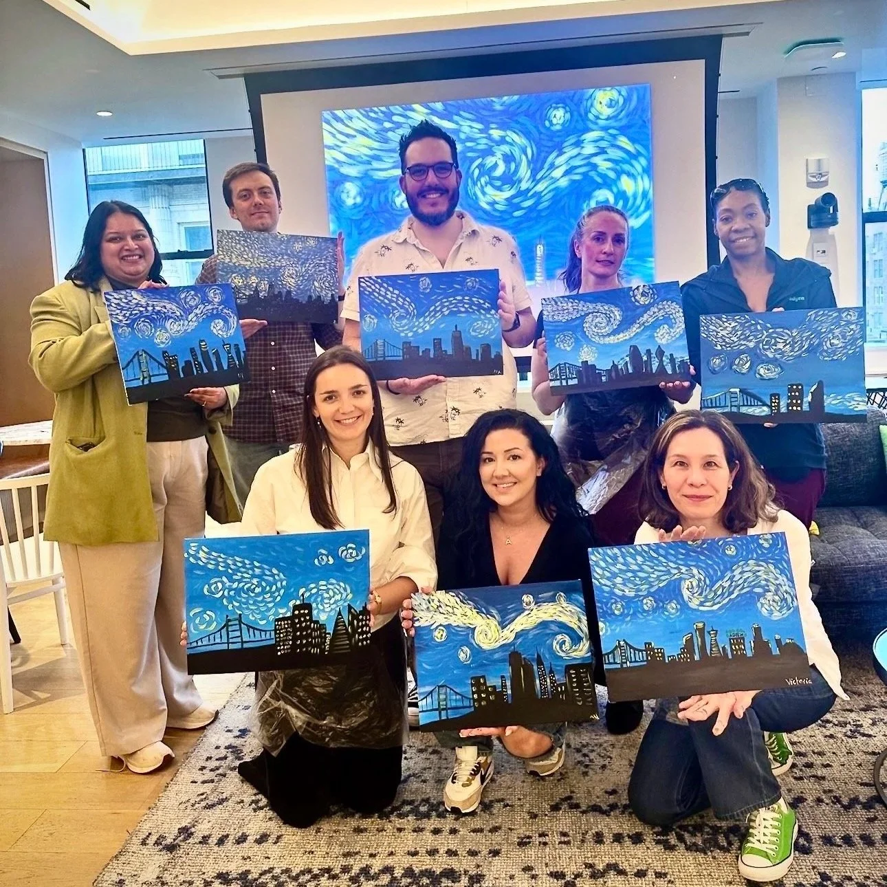 Participants displaying completed city skyline paintings during a ColorsintheDark painting class.