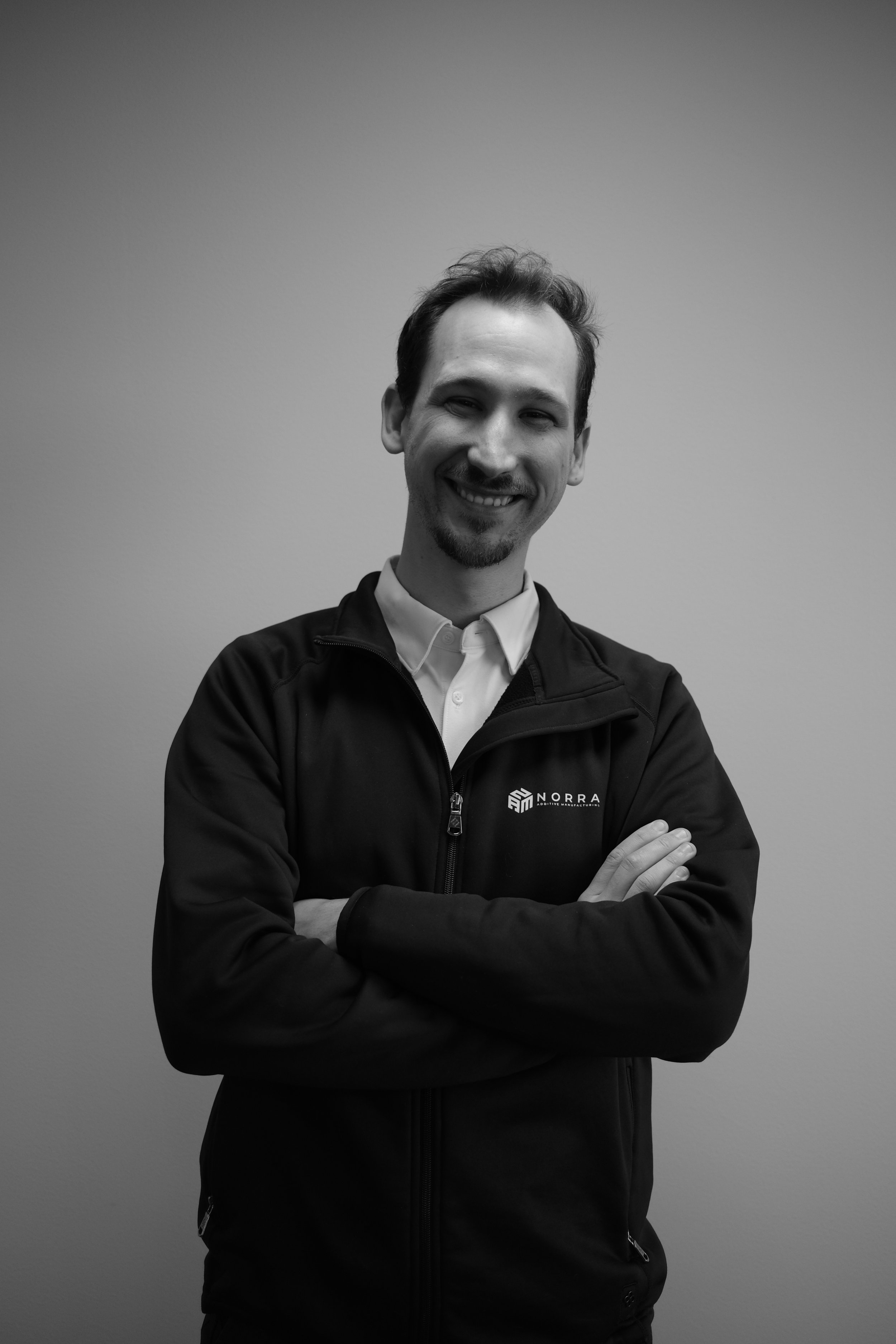Porträtt av Stefano, VD och ingenjör på Norra Additive Manufacturing, i ett svartvitt foto iklädd företagets jacka.