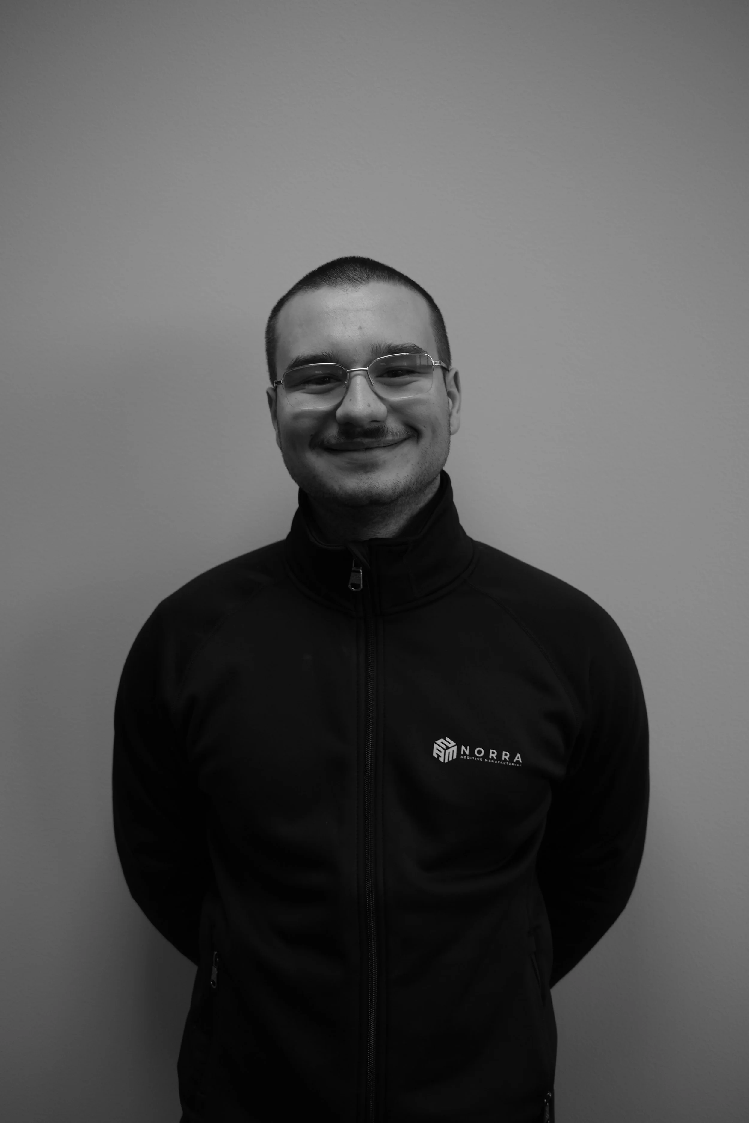 Porträtt av Martin, produktionsspecialist på Norra Additive Manufacturing, i svartvitt foto iklädd företagsjacka.