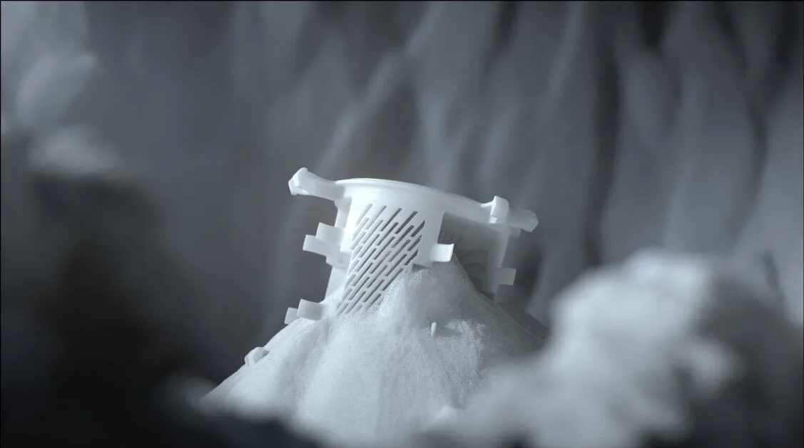 3D-utskriven polymerdel delvis täckt av pulver, vilket illustrerar fusionsprocessen i pulverbädden.