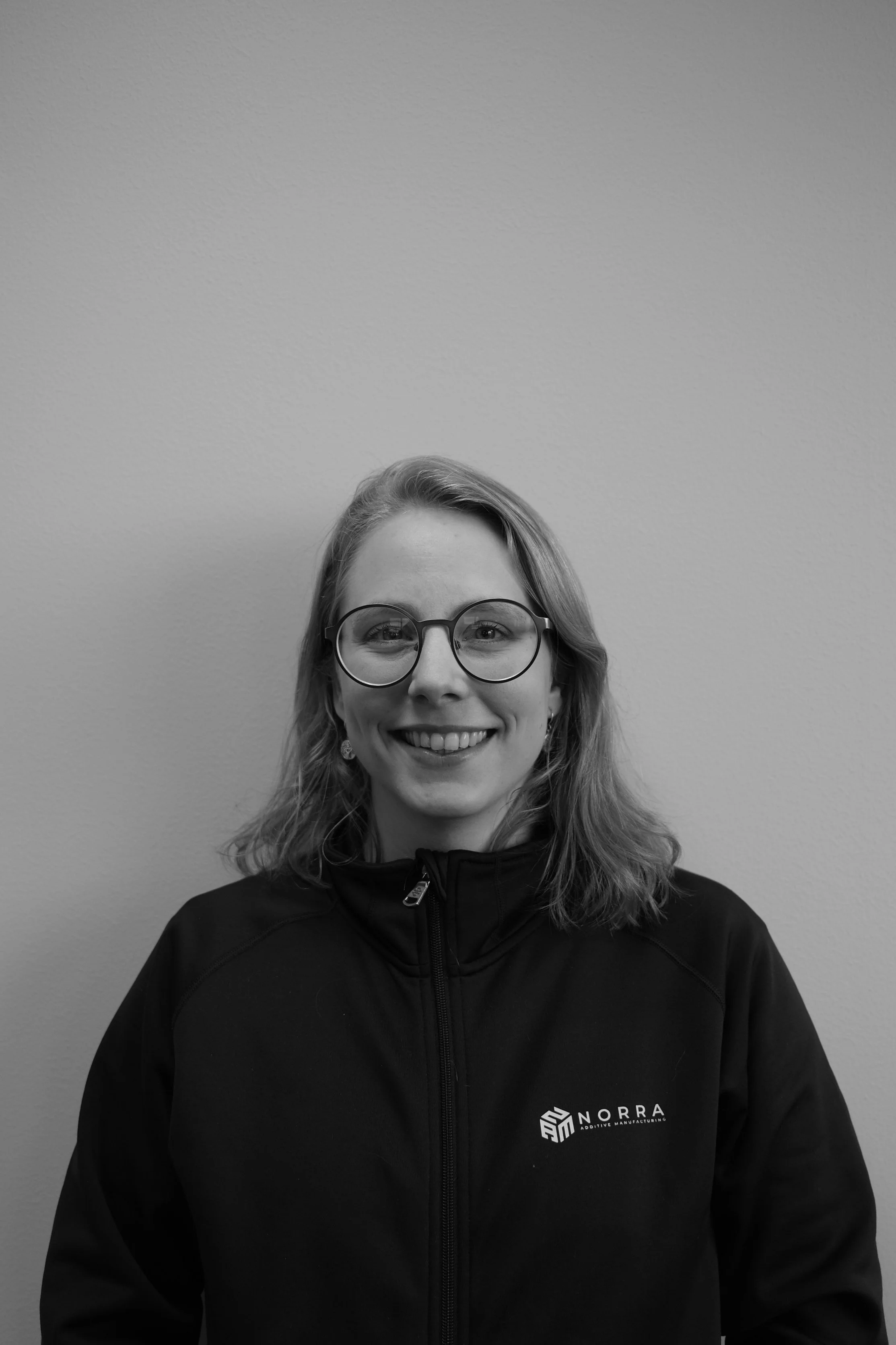 Porträtt av Denise, säljare på Norra Additive Manufacturing, i svartvitt foto iklädd företagsjacka.