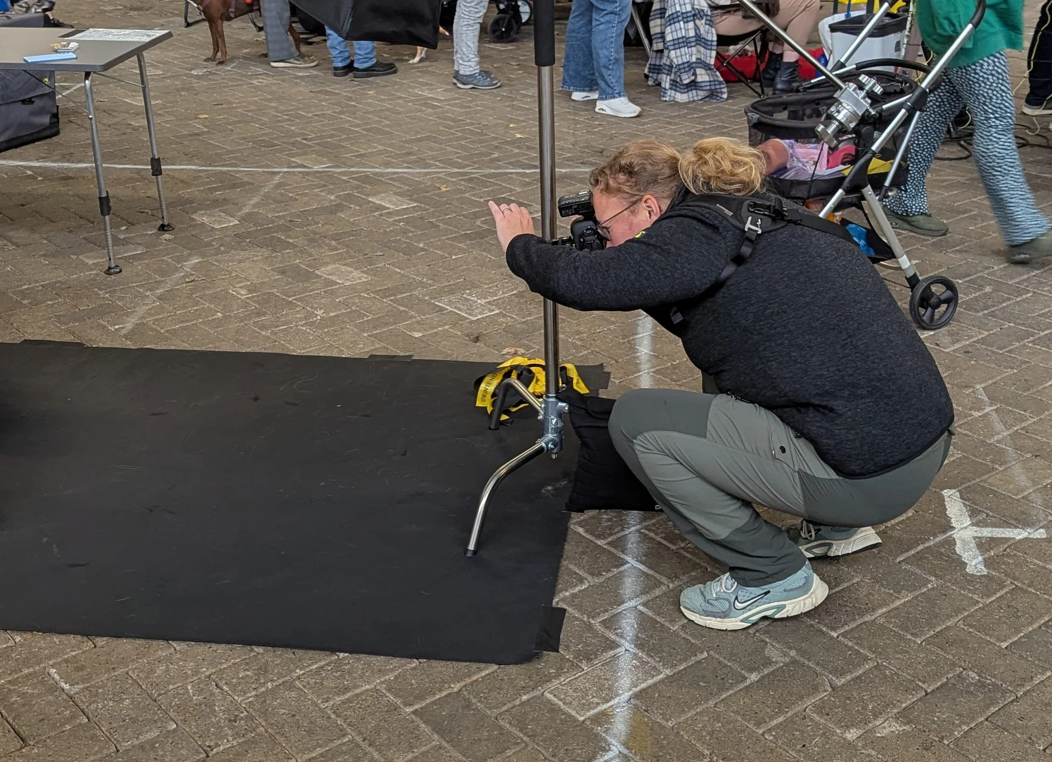 Een fotograaf met lang blond haar zit gehurkt met een camera voor een fotostudio op locatie.