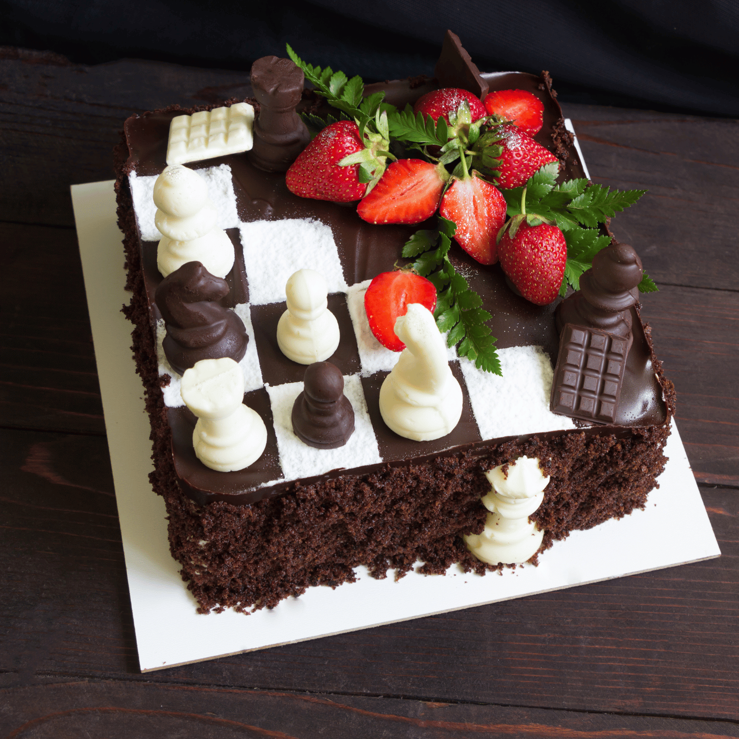 Chocolate cake designed as a chessboard with chocolate chess pieces and sliced strawberries on top.