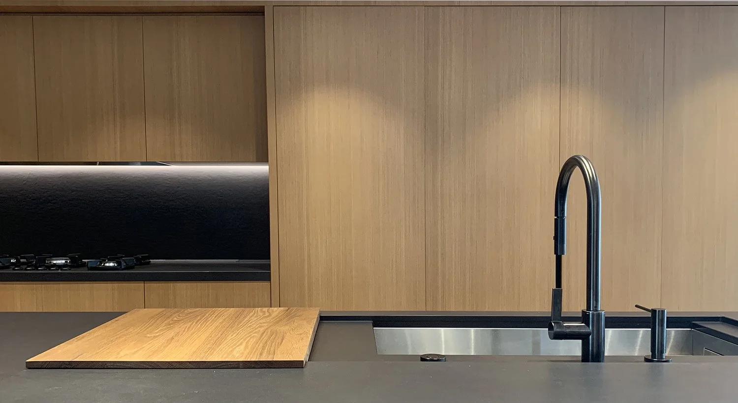 Modern kitchen design with natural wood cabinetry, black stone countertop