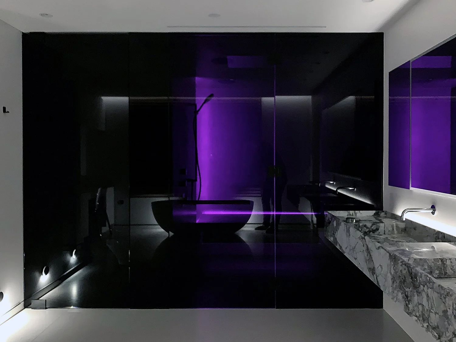 Modern luxury bathroom with black glass shower, purple LED lighting