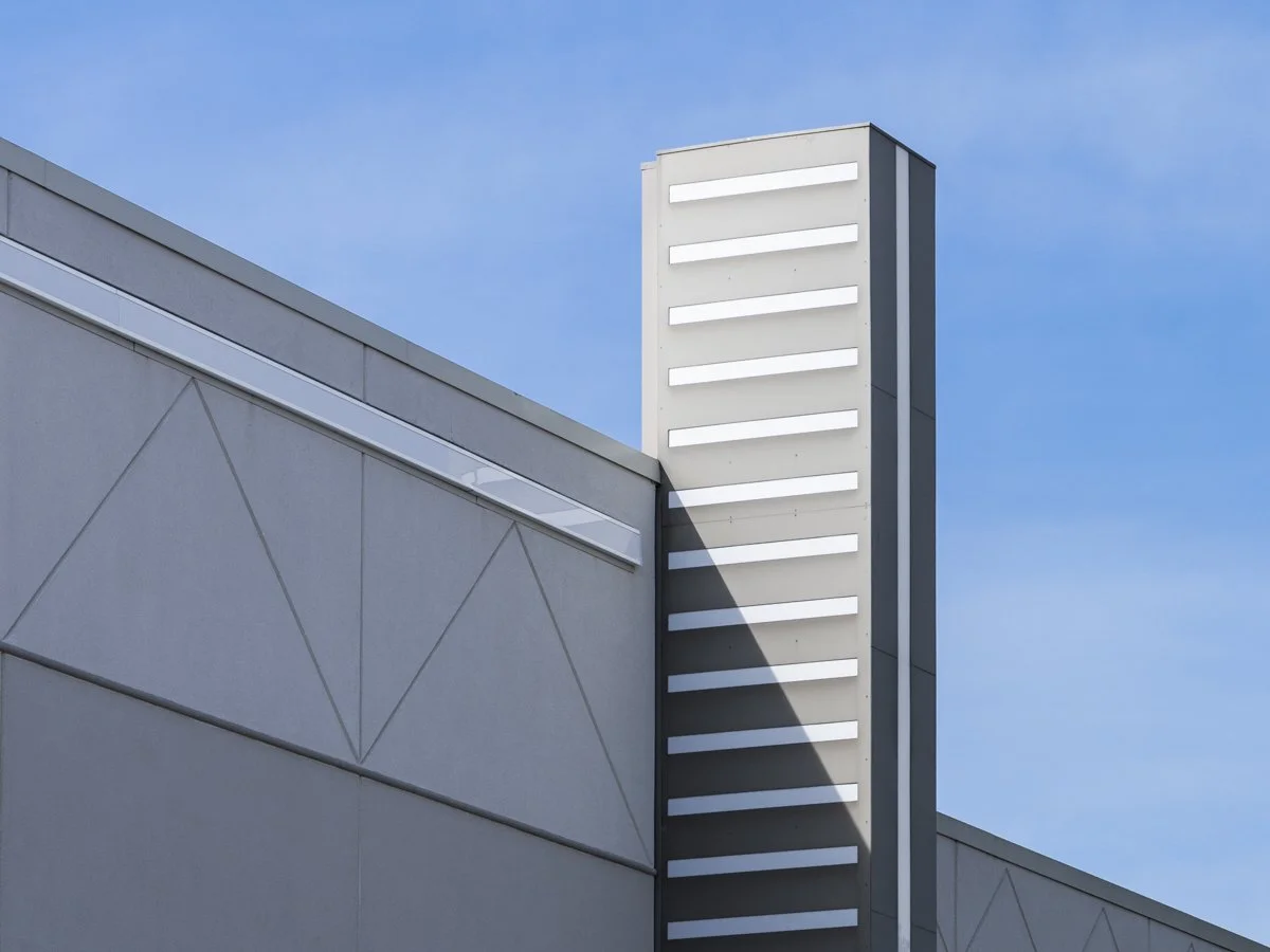 Modern building with geometric wall design and a vertical white slatted feature against a blue sky.