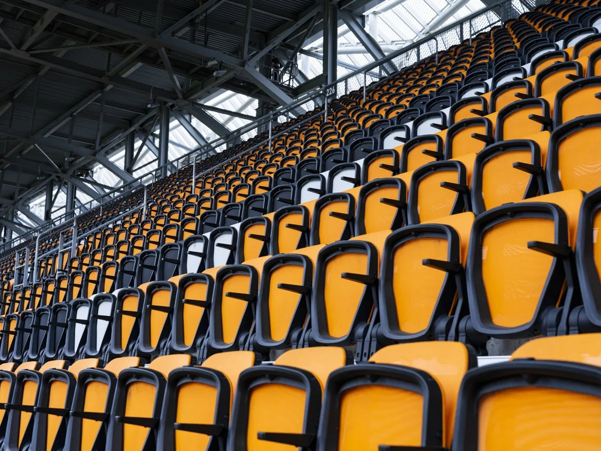 Empty orange and black stadium seats in a large sports arena.