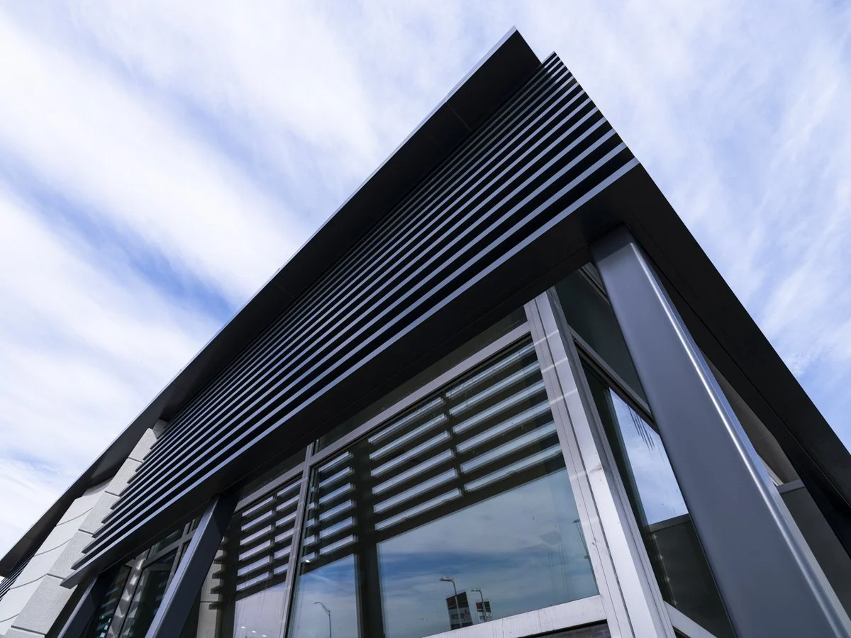 Low-angle view of a modern building with black horizontal louvers and glass windows against a cloudy sky.
