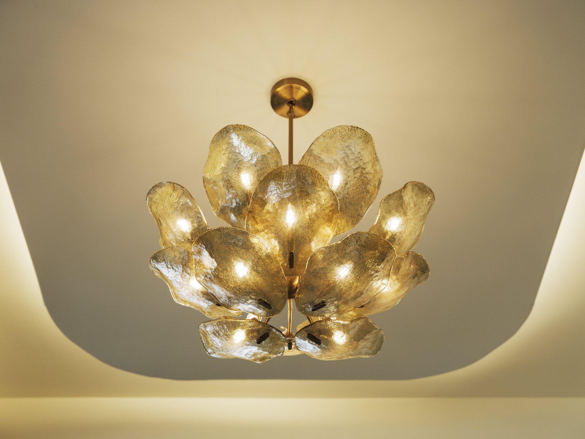 Elegant chandelier with multiple gold-toned glass petals hanging from ceiling with warm lighting