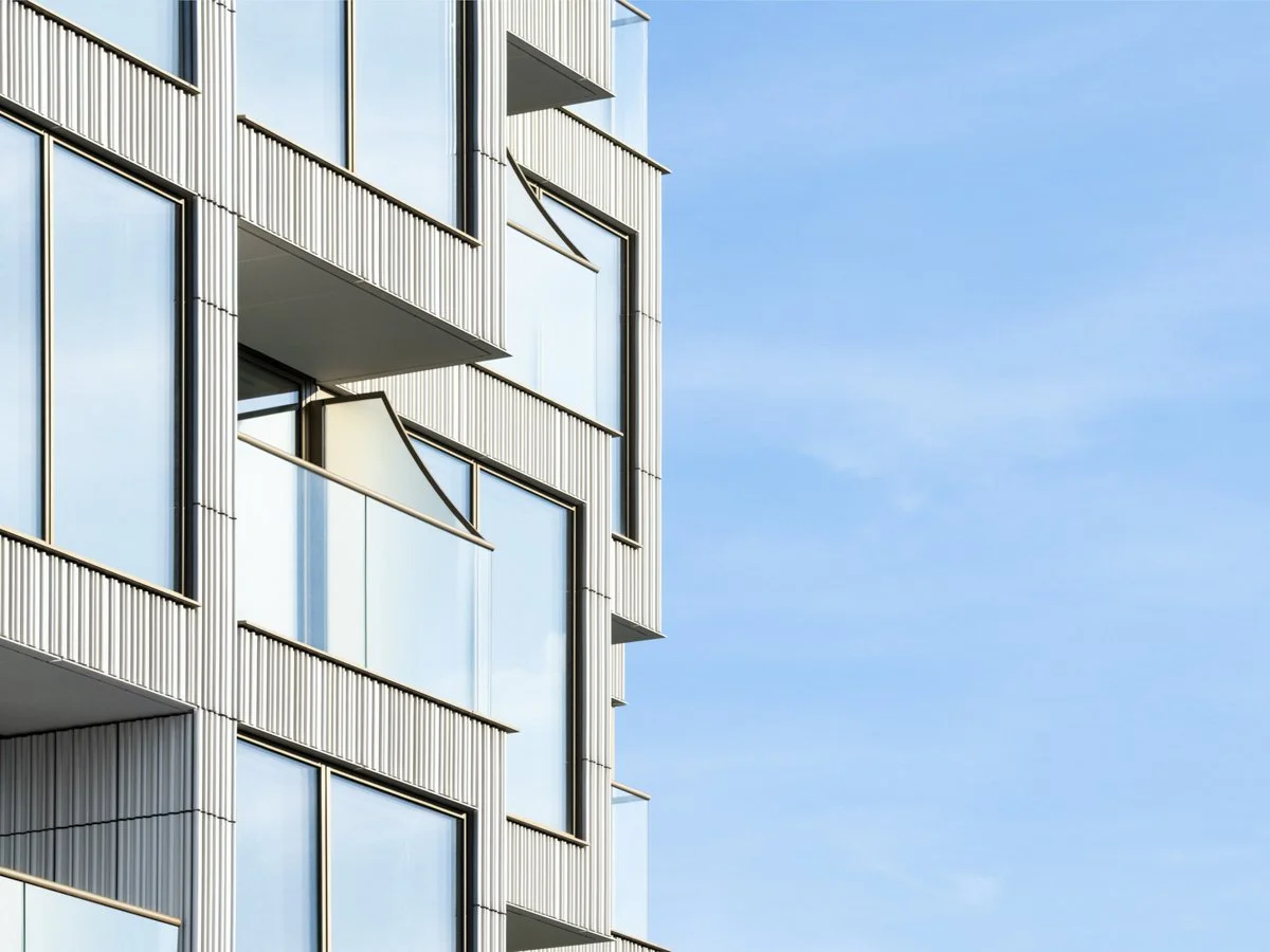 Close-up of a modern building with glass windows and metallic exterior panels against a blue sky.
