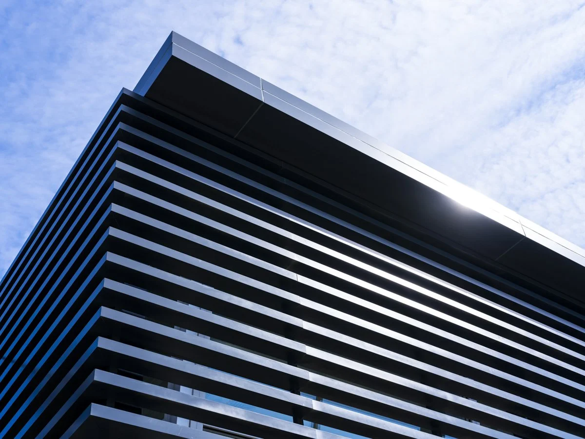 Close-up of a modern building with horizontal black and white stripes, against a cloudy sky.