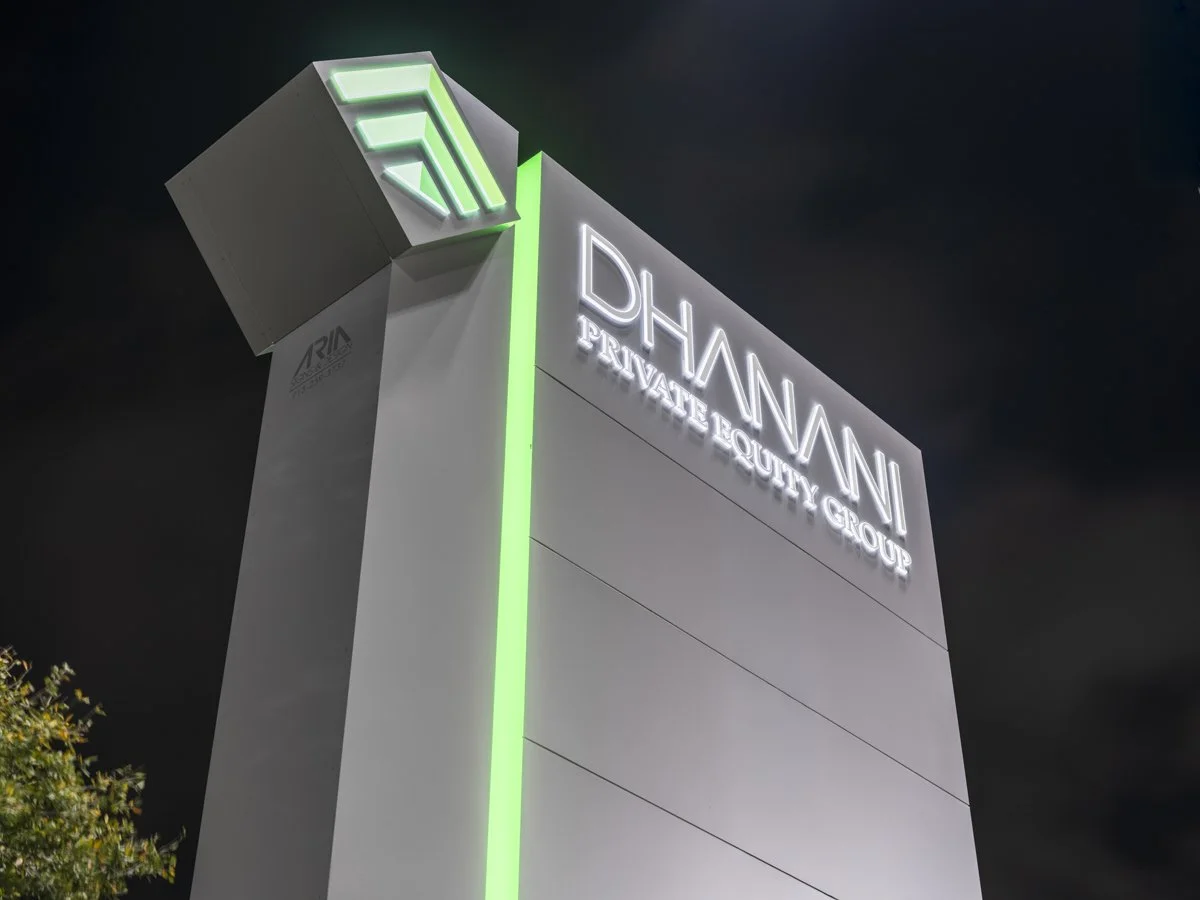 Nighttime view of a tall, modern building with illuminated sign reading 'DHANNI PARAMAT?EQUITY GROUP' and a green and white logo at the top.