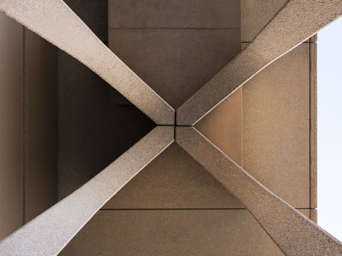 View of a building's overhang from below, showing symmetrical geometric lines and shapes with brown and beige tones.