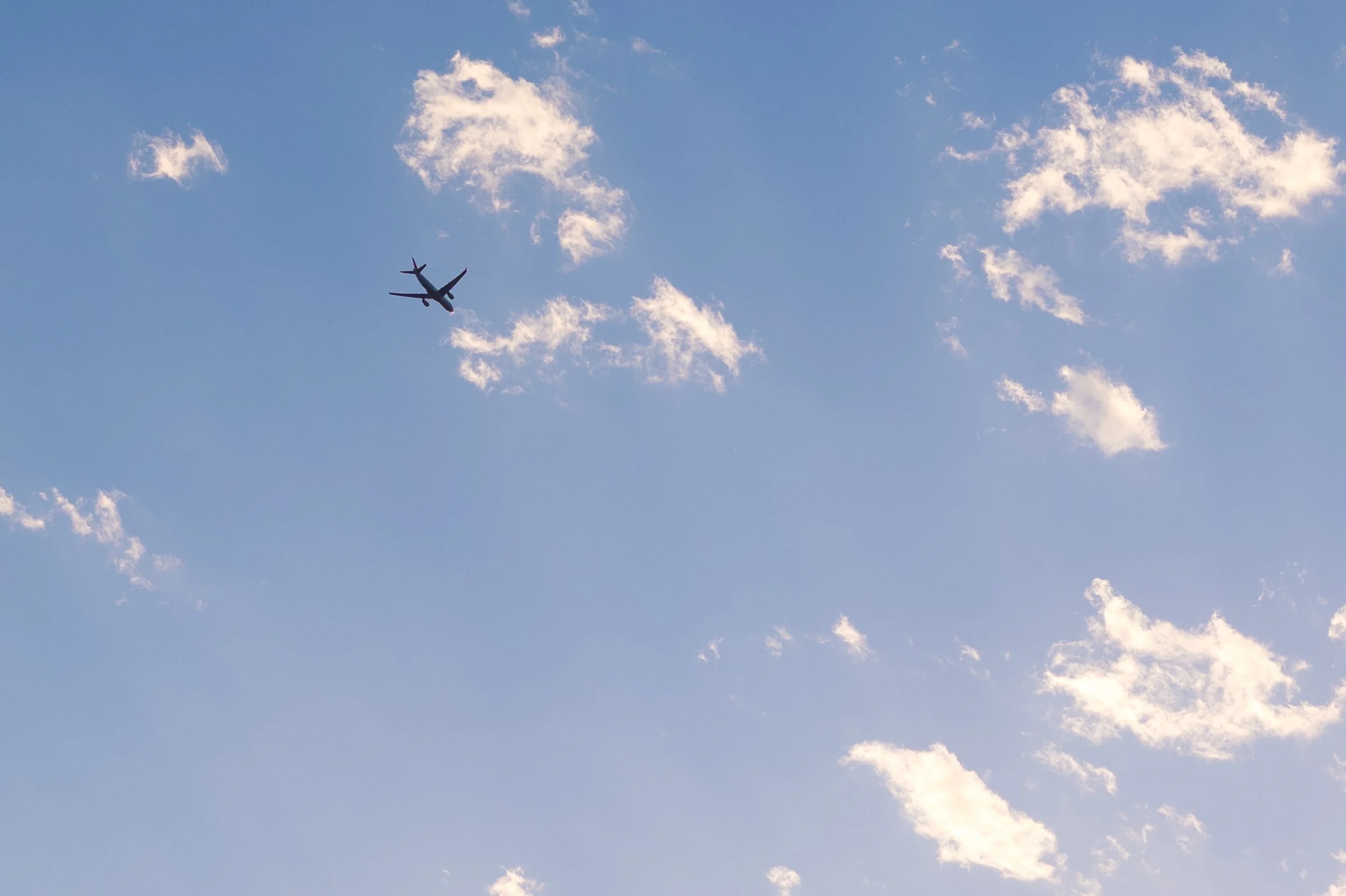 An airplane flying in a blue sky with scattered white clouds.